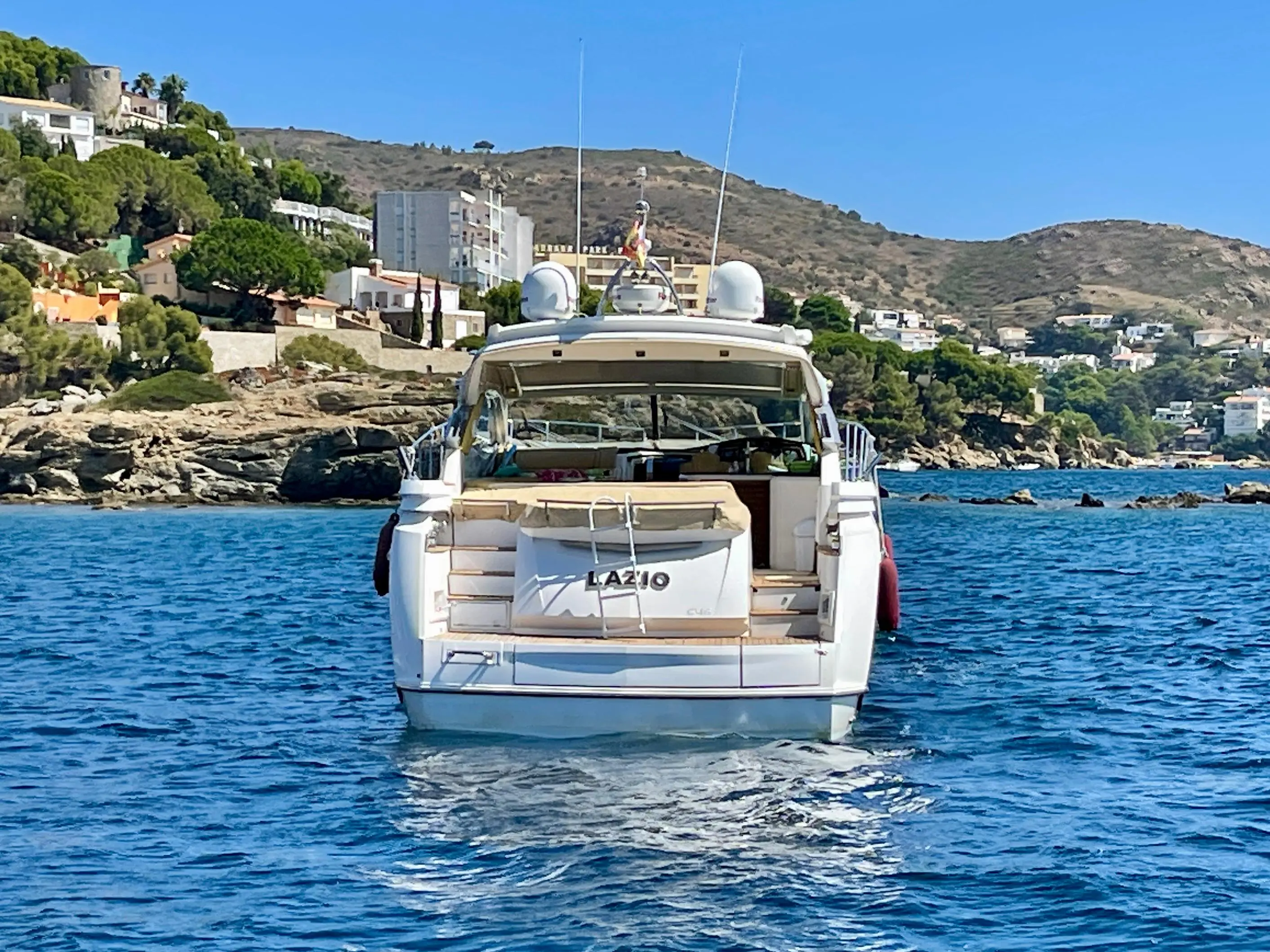 Sessa Marine C46 — Vue arrière d’un bateau à moteur naviguant près d’une côte rocheuse.