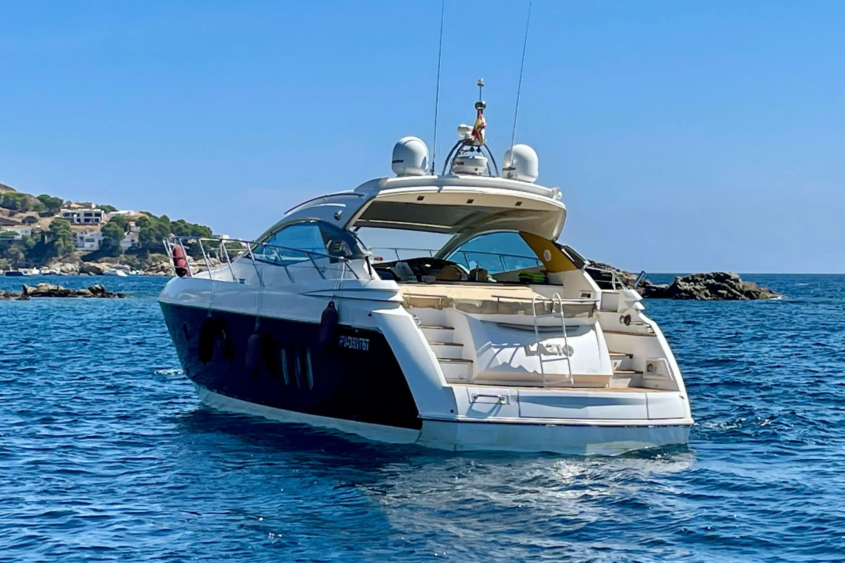 Sessa Marine C46 — Bateau à moteur vu de trois quarts arrière, naviguant près d’une côte rocheuse.