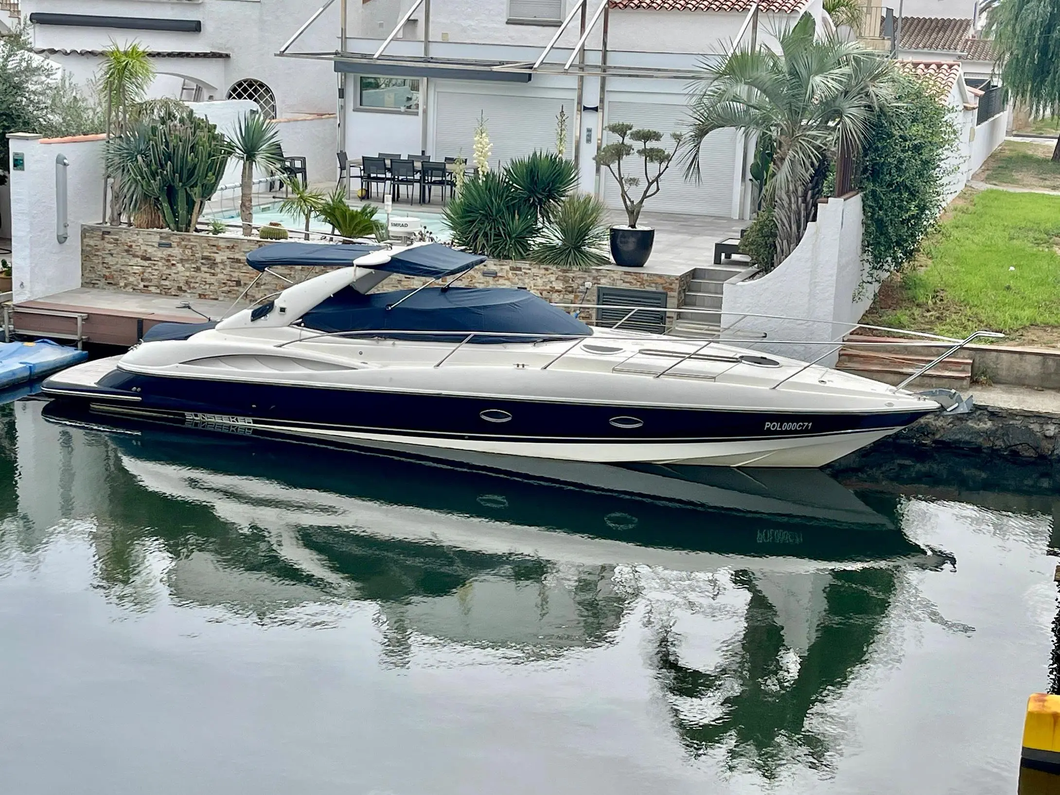 Sunseeker Superhawk 40 — Bateau à moteur blanc et bleu amarré devant une villa, vu de profil.