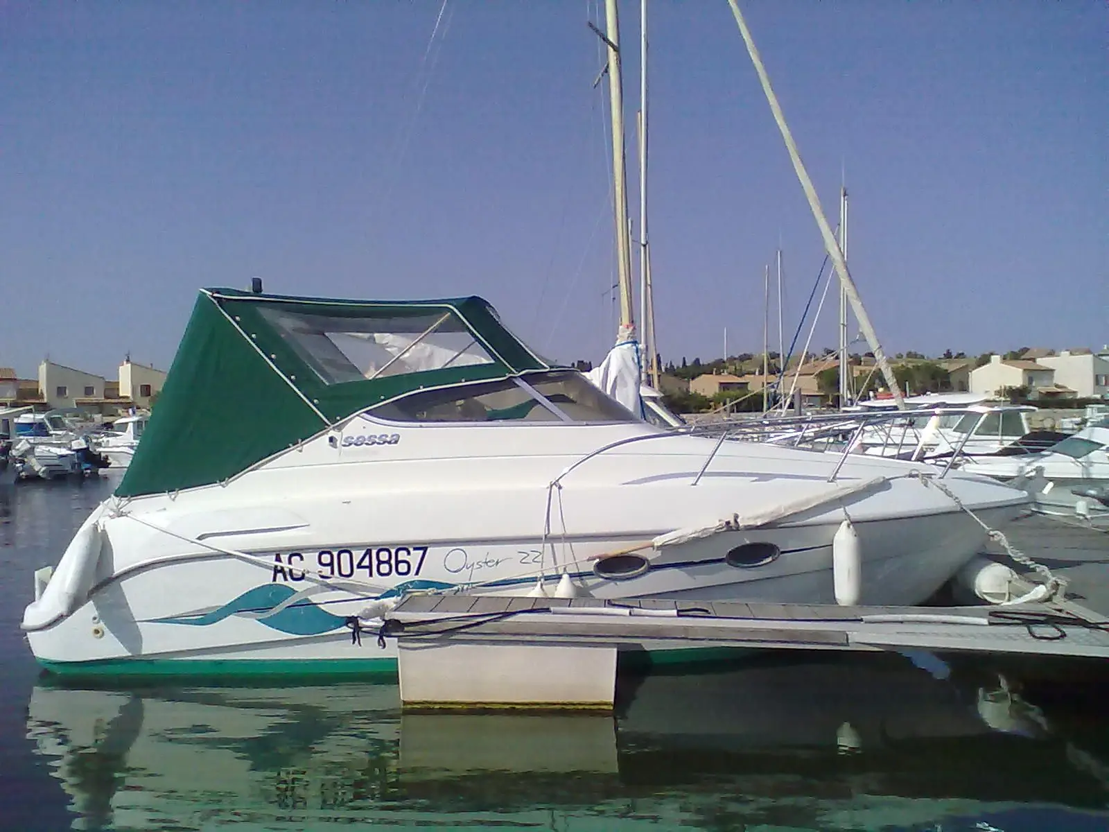 Sessa Marine Oyster 22 — Bateau à moteur blanc amarré dans un port, avec taud vert et pare-battages.