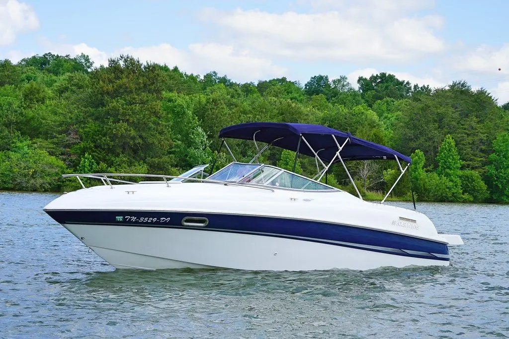 Four Winns Sundowner 225 — Bateau à moteur blanc et bleu photographié sur un lac, sous une toile de cockpit.