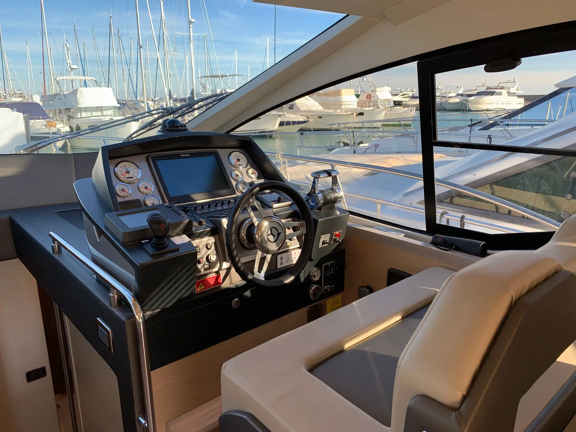 Queens Yachts 50 HT — Poste de pilotage intérieur avec instruments, volant et vue sur le port.