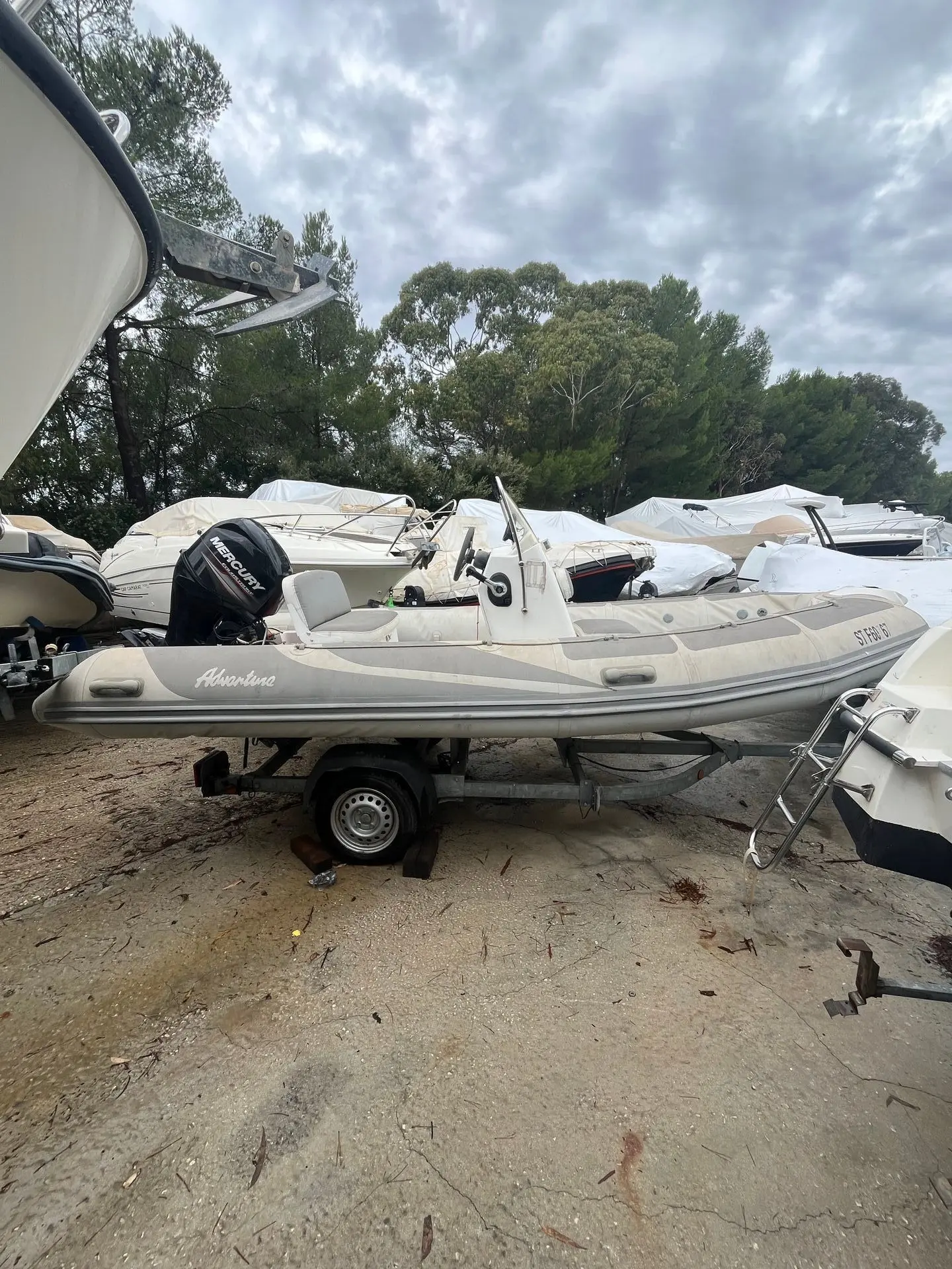 Adventure V-550 — Bateau pneumatique gris sur remorque, photographié à terre parmi d'autres embarcations.