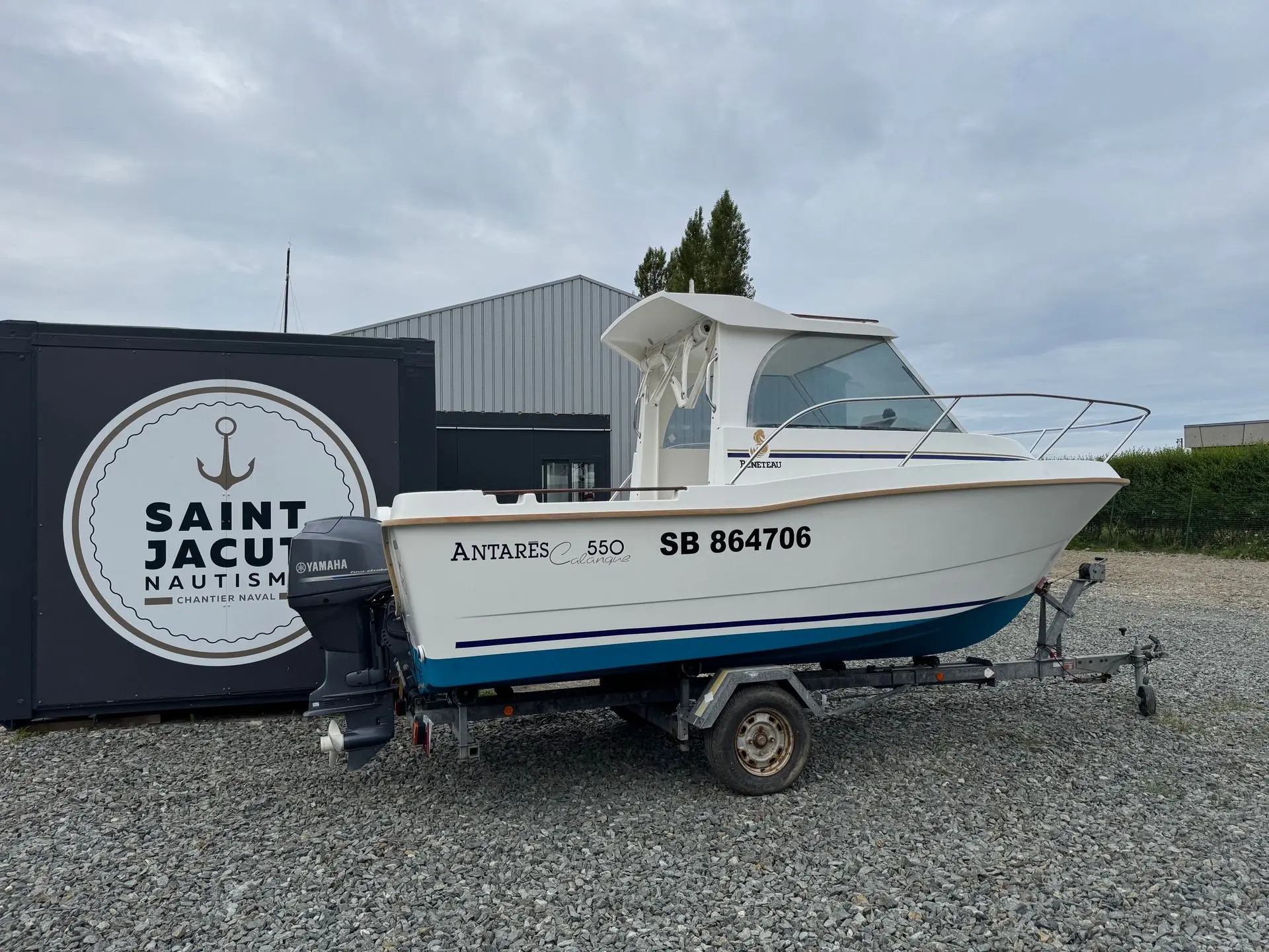 Beneteau Antares 550 — Bateau à moteur blanc exposé sur une remorque devant un chantier naval.