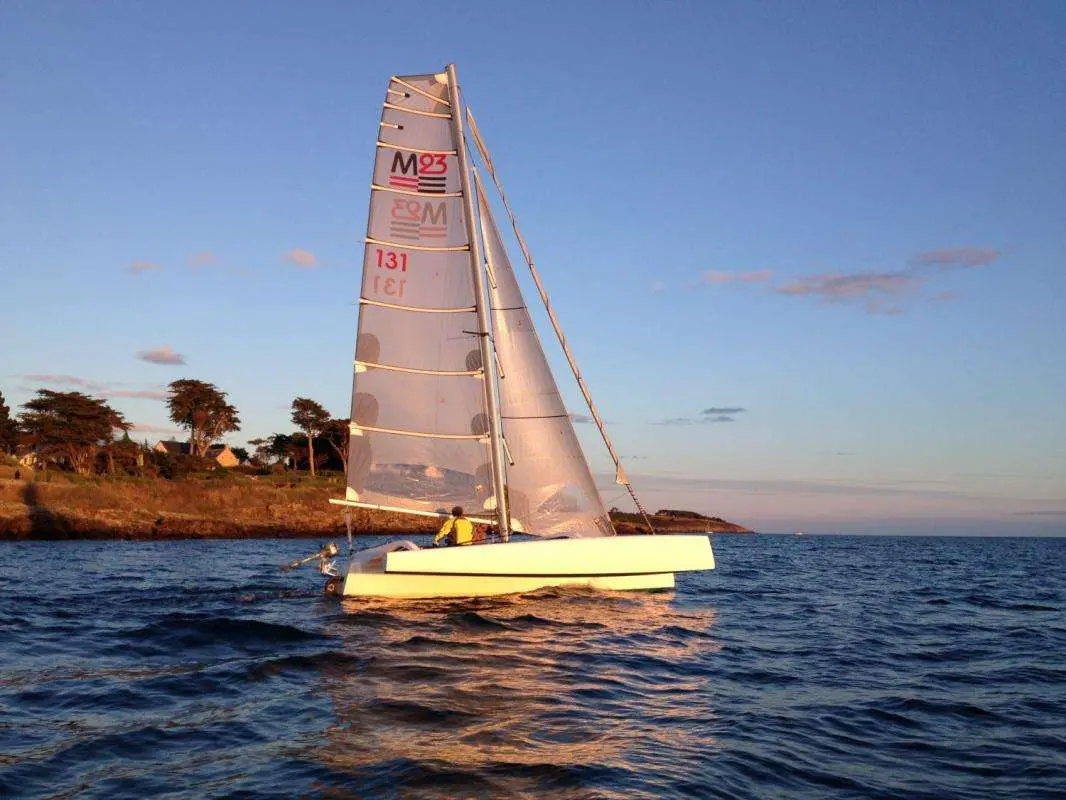 Torpen Multi 23 Trimaran — Catamaran à voile naviguant près d’une côte au coucher du soleil.