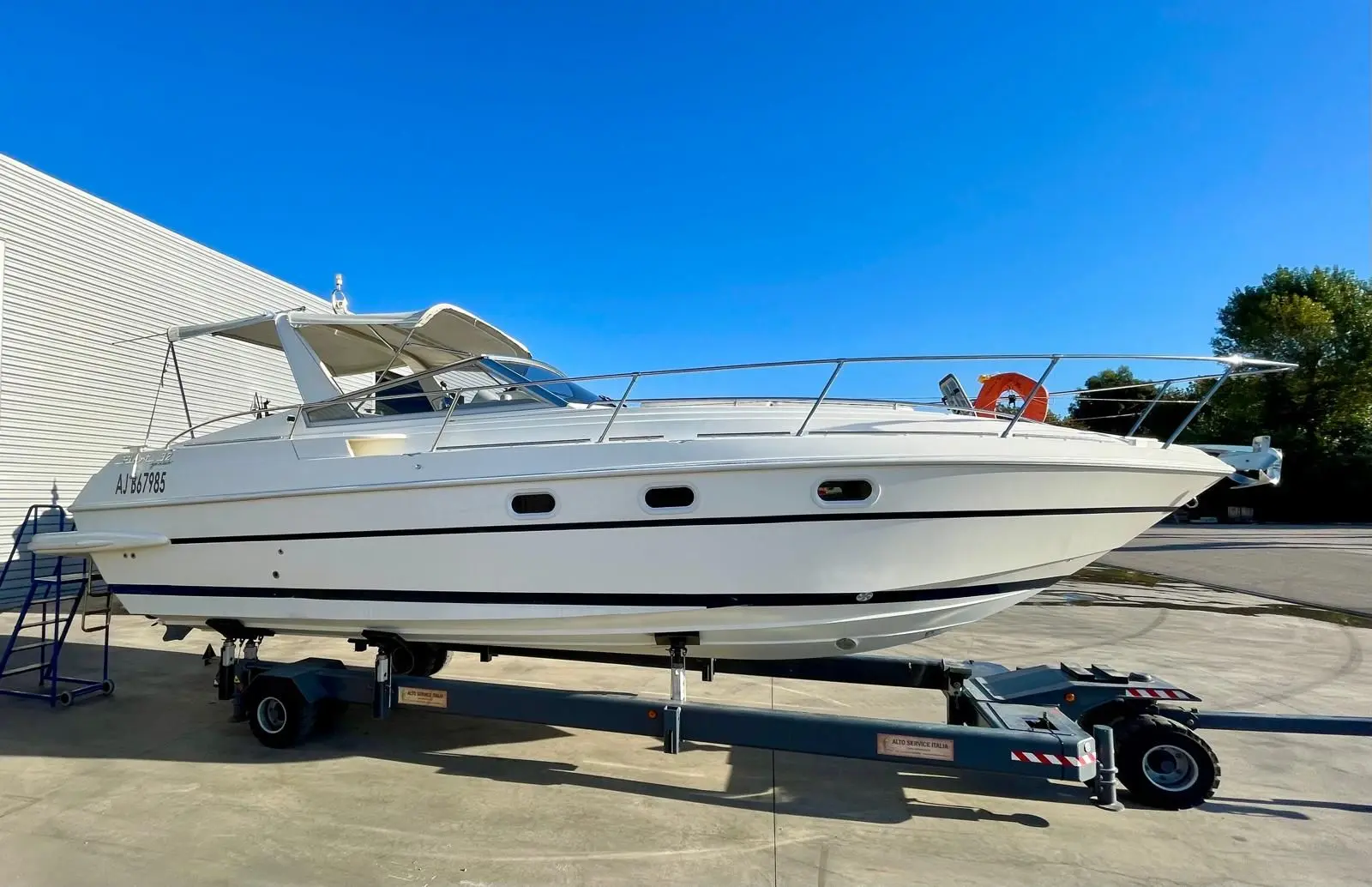 Fiart Mare Fiart 32 Genius — Bateau à moteur blanc vu de profil sur remorque, à terre devant un bâtiment.