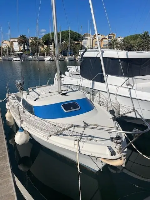 Yachting France Jouet 540 — Voilier amarré vu de l’avant, avec coque blanche et rouf bleu.