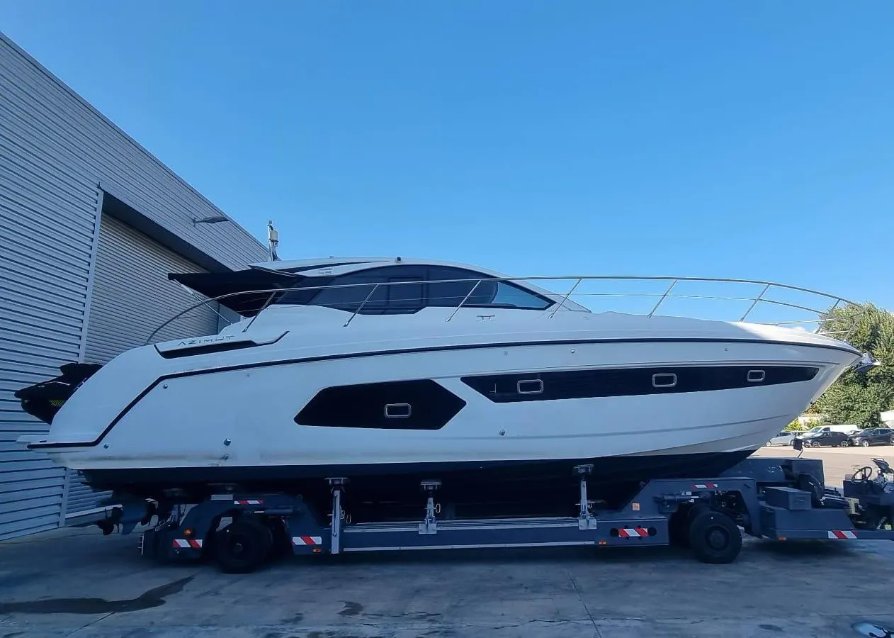 Azimut Atlantis 43 — Bateau à moteur blanc vu de profil, posé sur une remorque devant un bâtiment.