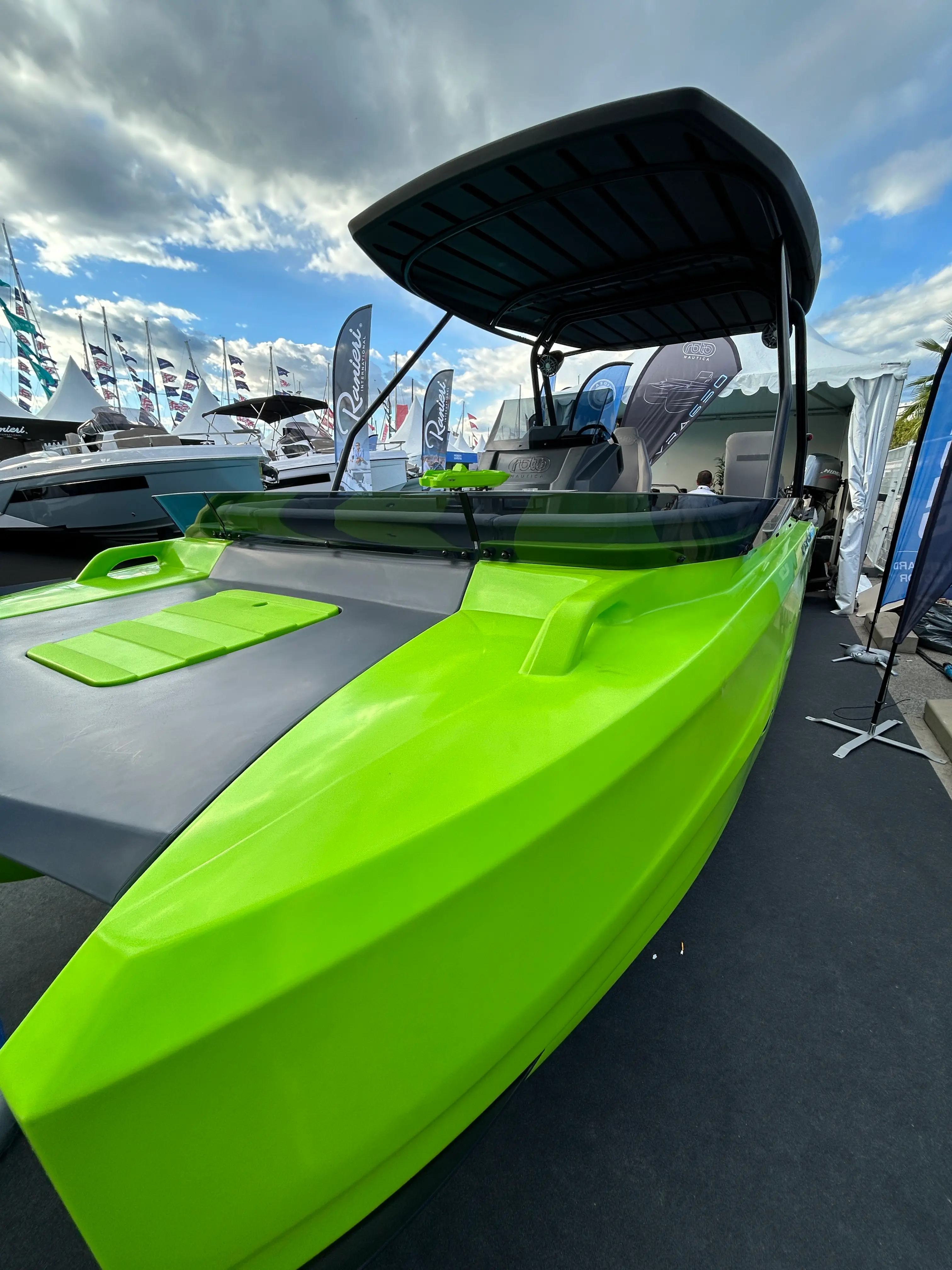 Roto Korkyra — Bateau vert exposé sur un stand nautique, vu de l’avant avec console et taud.