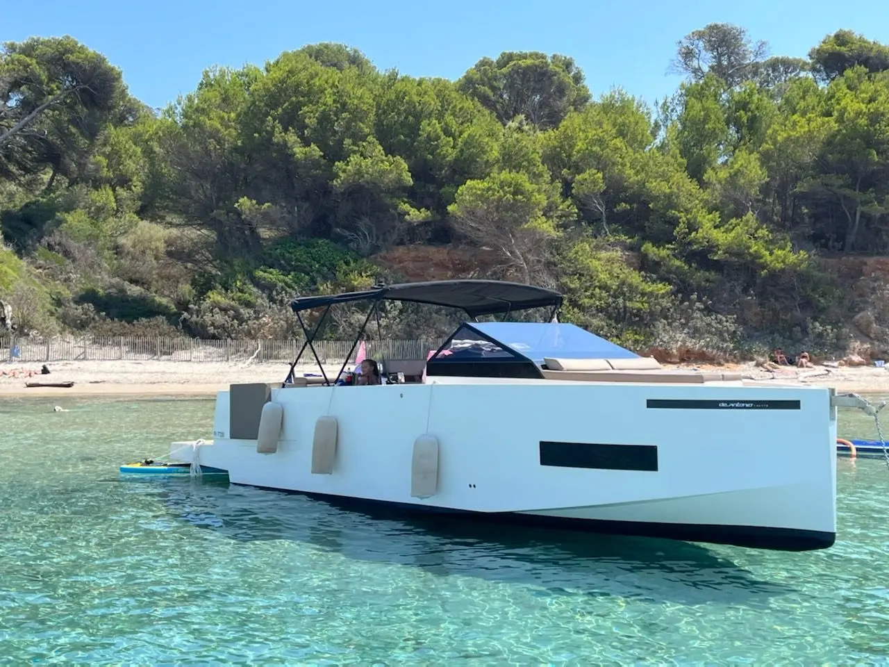 De Antonio Yachts D33 Cruiser — Bateau à moteur blanc vu de trois quarts, amarré près d’une plage arborée.