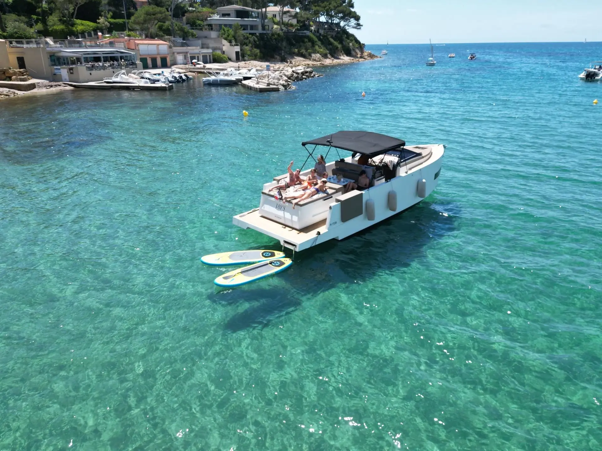 De Antonio Yachts D33 Cruiser — Bateau à moteur blanc vu de trois quarts arrière dans une baie turquoise.