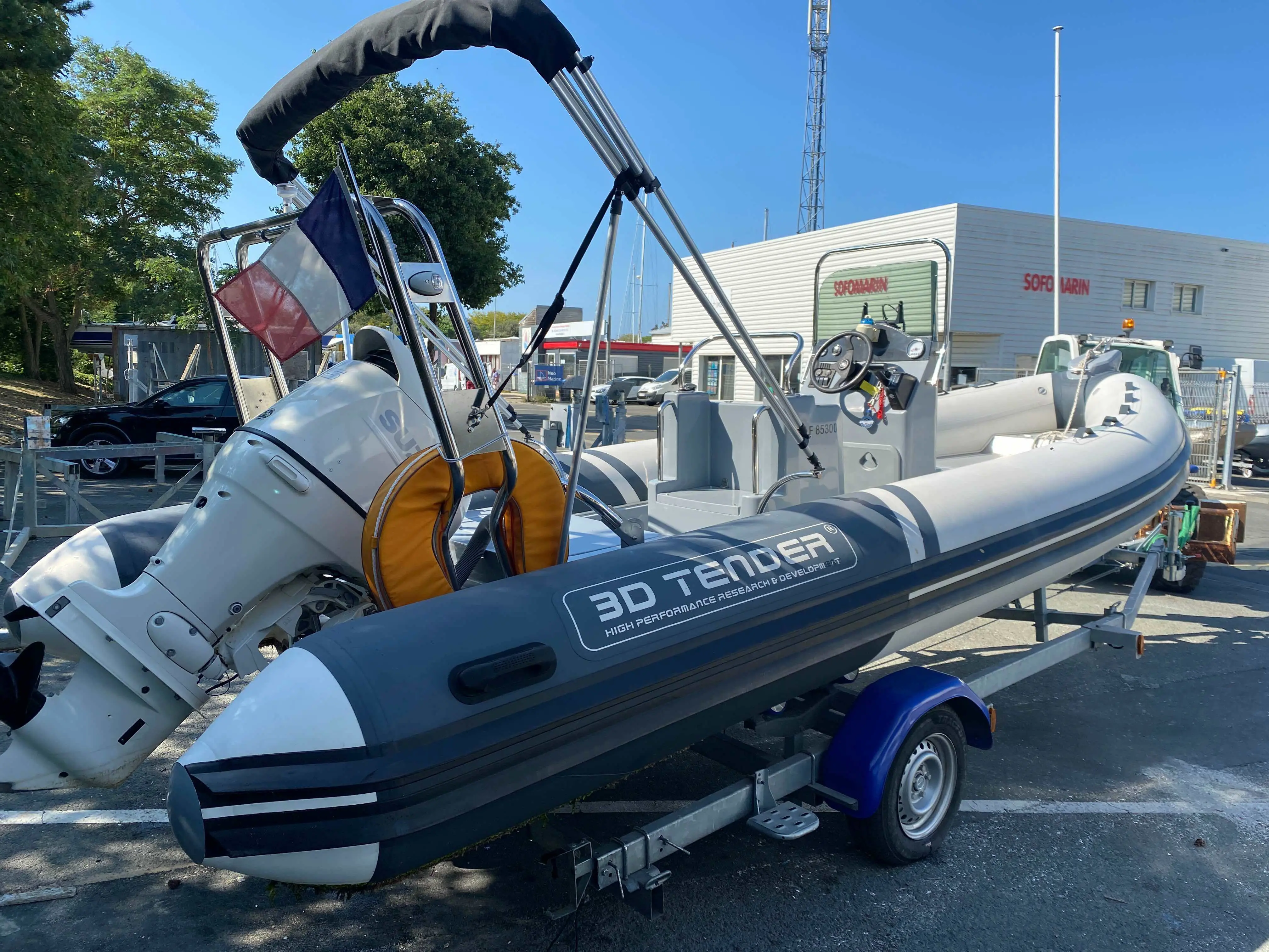 3D Tender Lux 635 — Bateau pneumatique gris avec moteur hors-bord, console centrale et arceau sur remorque.