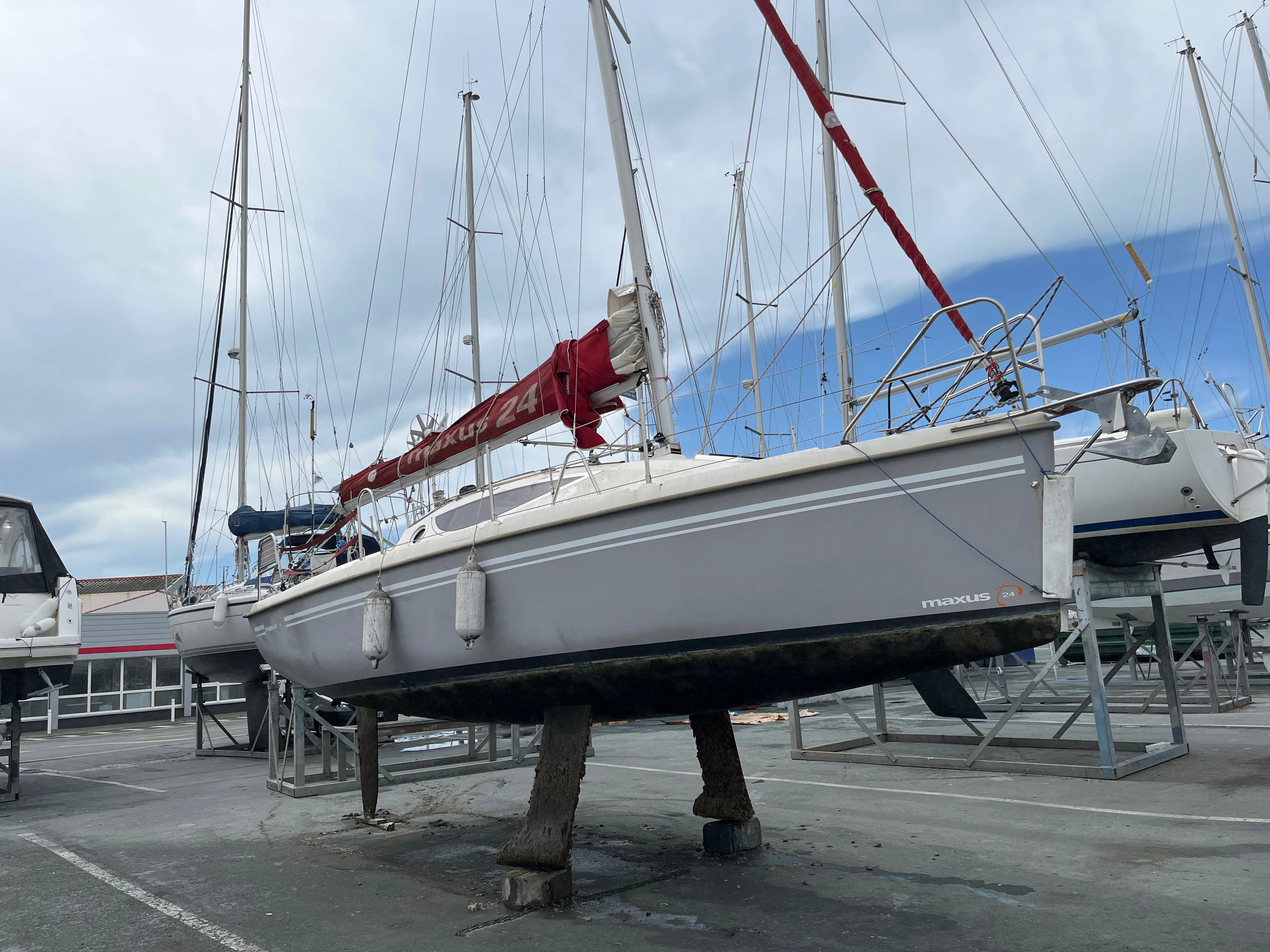 Maxus 24 — Voilier gris photographié à terre sur berceau, avec son mât et ses voiles ferlées.