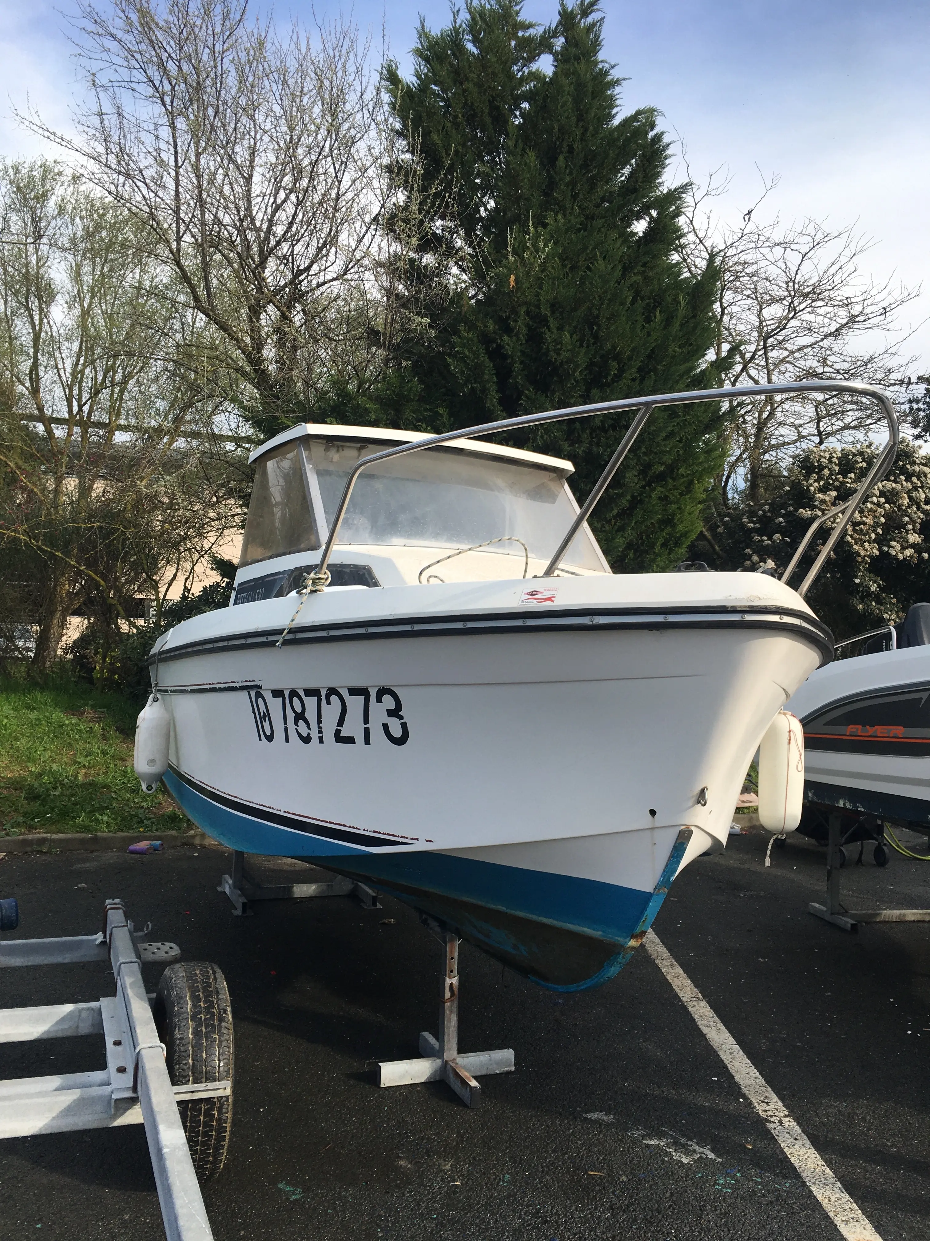 Jeanneau Esteou 530 — Bateau à moteur blanc et bleu photographié sur sa remorque à terre.