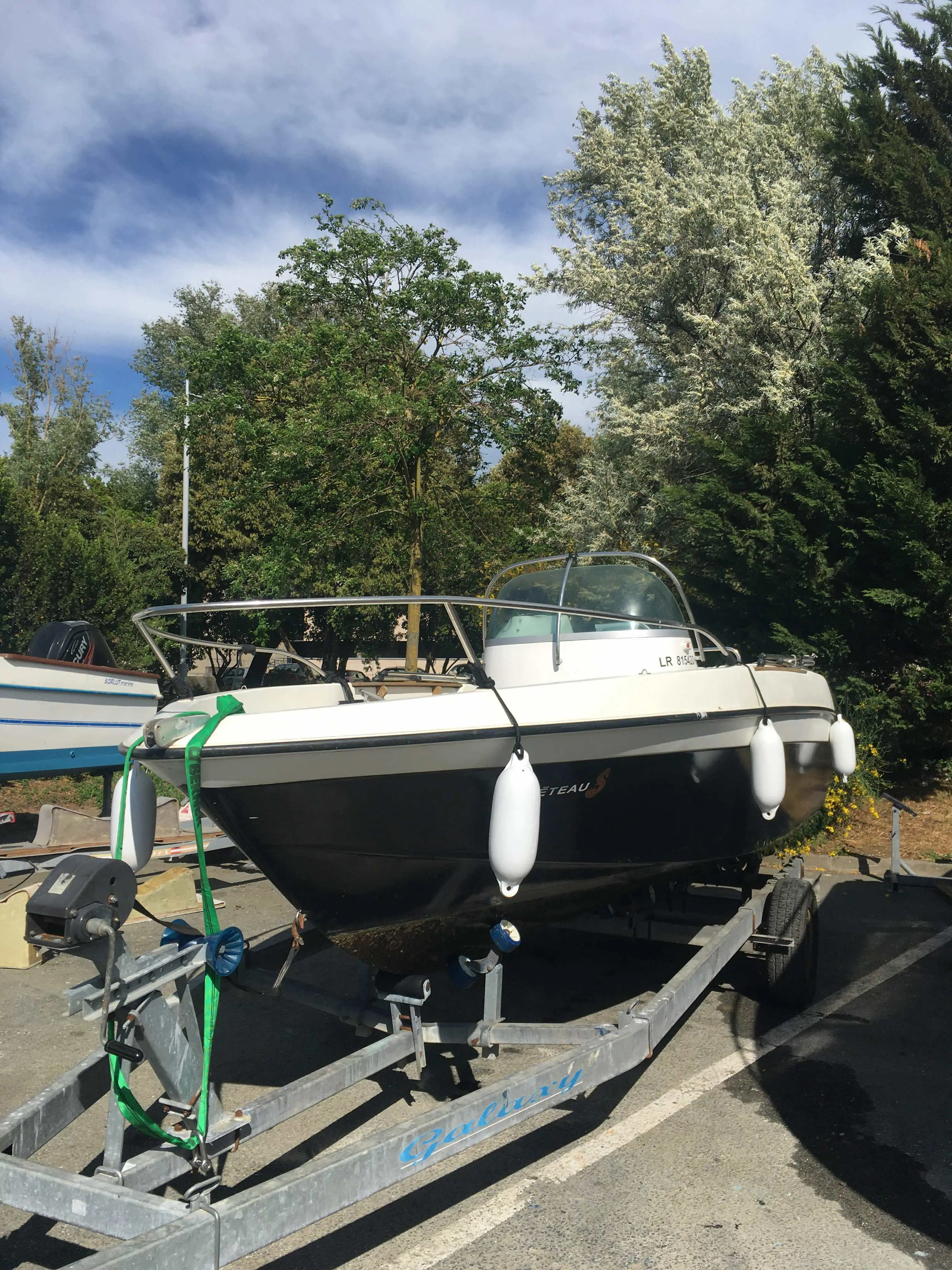 Beneteau Flyer 560 — Bateau à moteur blanc et noir posé sur une remorque, dans un espace arboré.