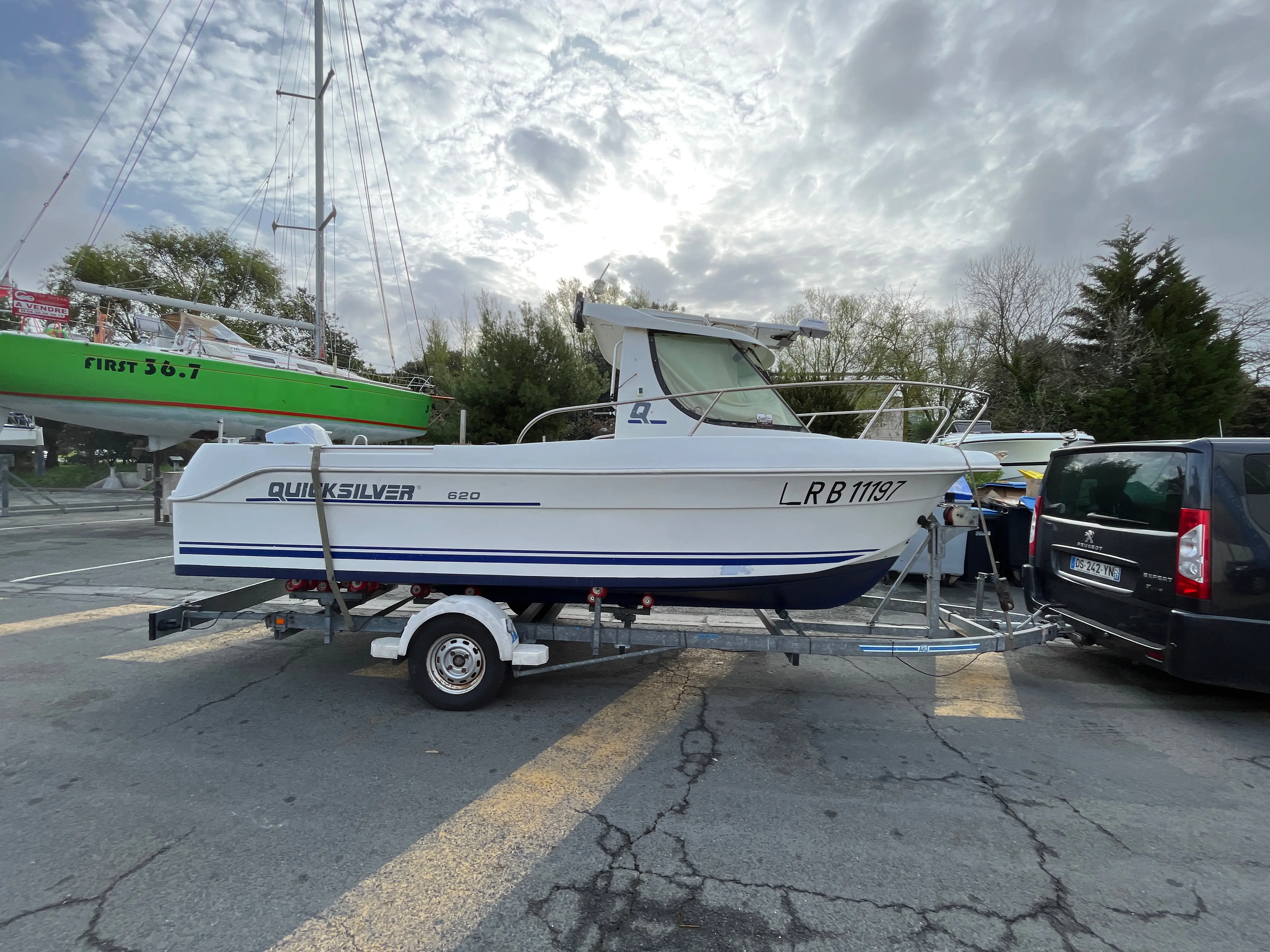 Quicksilver 620 Open — Bateau blanc à cabine présenté sur remorque, photographié de profil sur un parking.