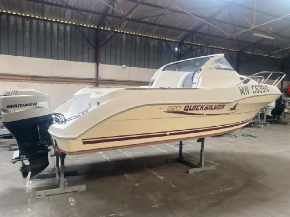 Quicksilver 620 Open — Bateau à moteur blanc vu de trois quarts, sur berceau, dans un hangar.