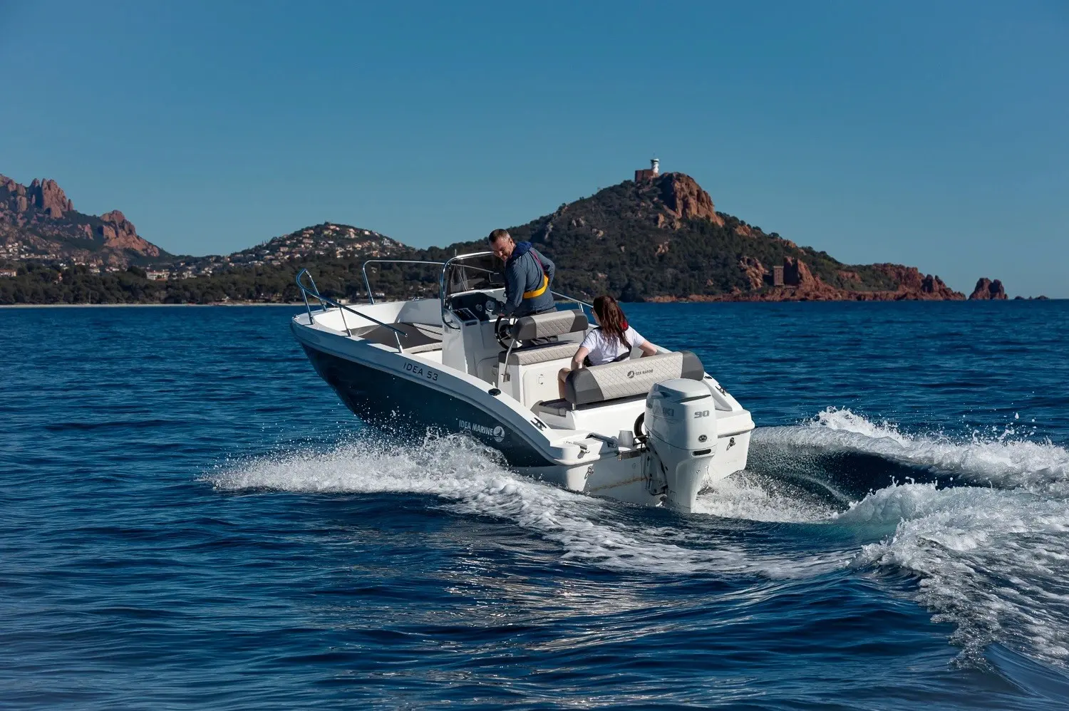 Idea Marine 530 Open — Bateau à moteur naviguant au large d’une côte rocheuse, vu de trois quarts arrière.