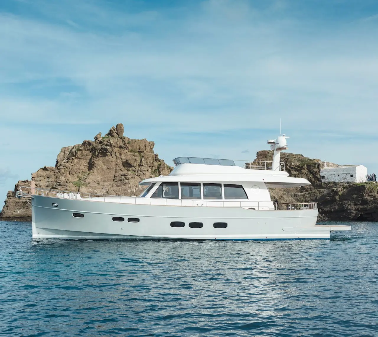 Sasga Menorquin 68 — Bateau à moteur blanc vu de profil devant une côte rocheuse.