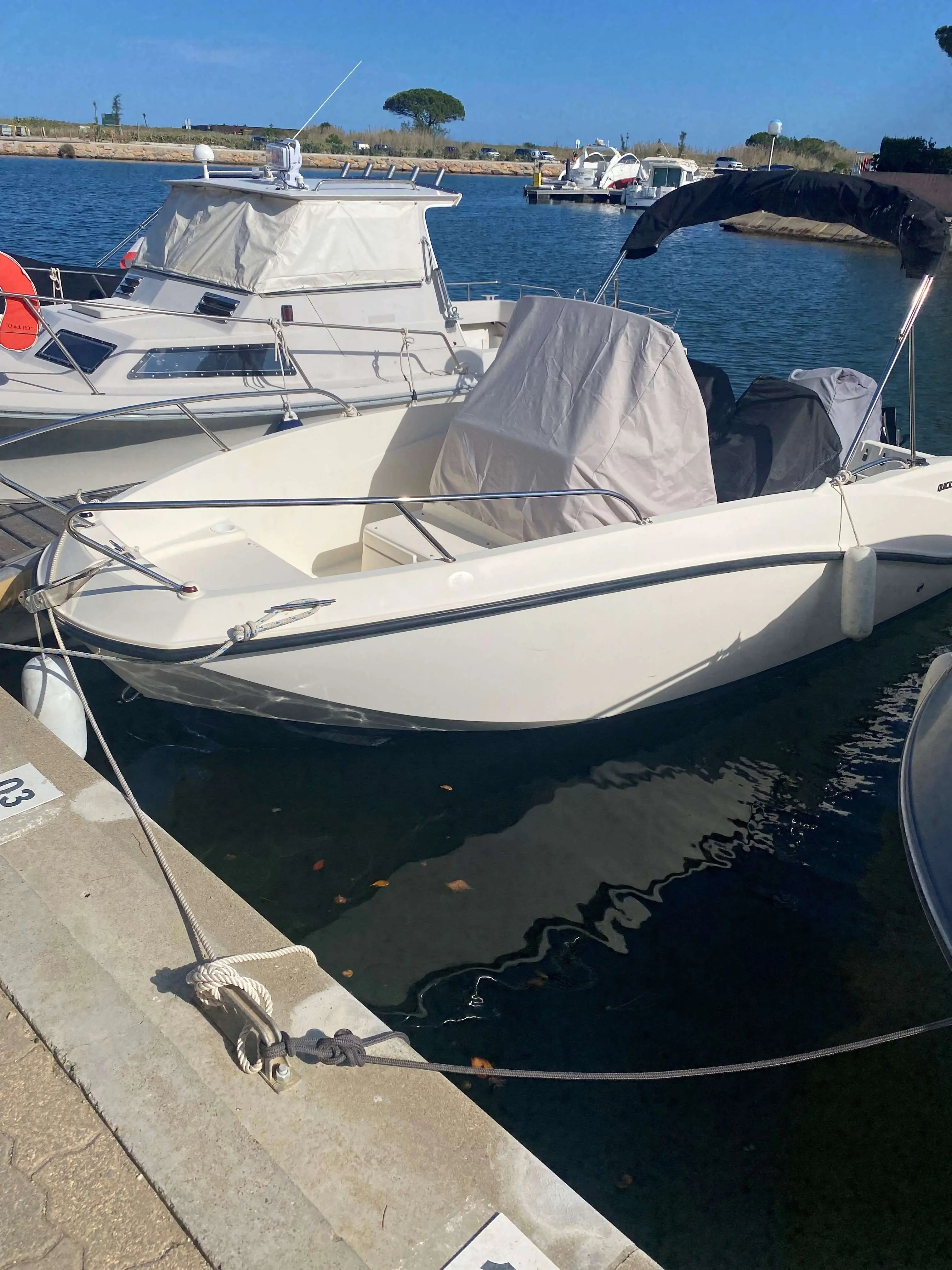 Quicksilver Activ 535 Open — Bateau blanc amarré dans un port, avec plusieurs équipements protégés par des bâches.