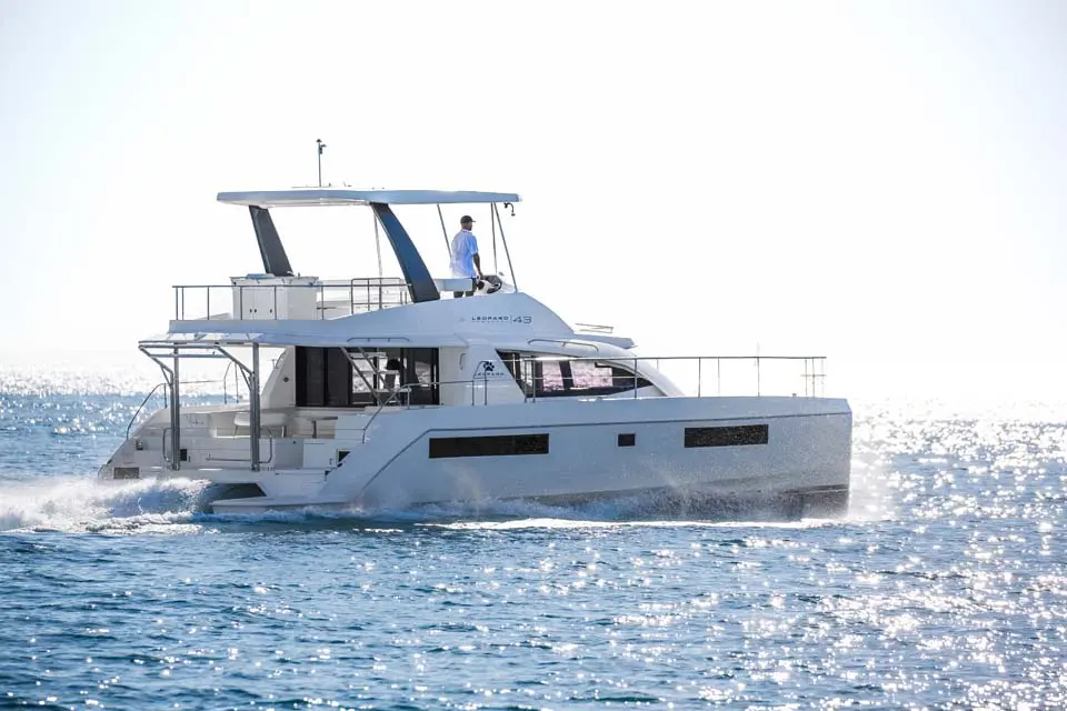 Leopard 43 — Catamaran à moteur blanc vu de profil sur une mer scintillante, avec une personne.