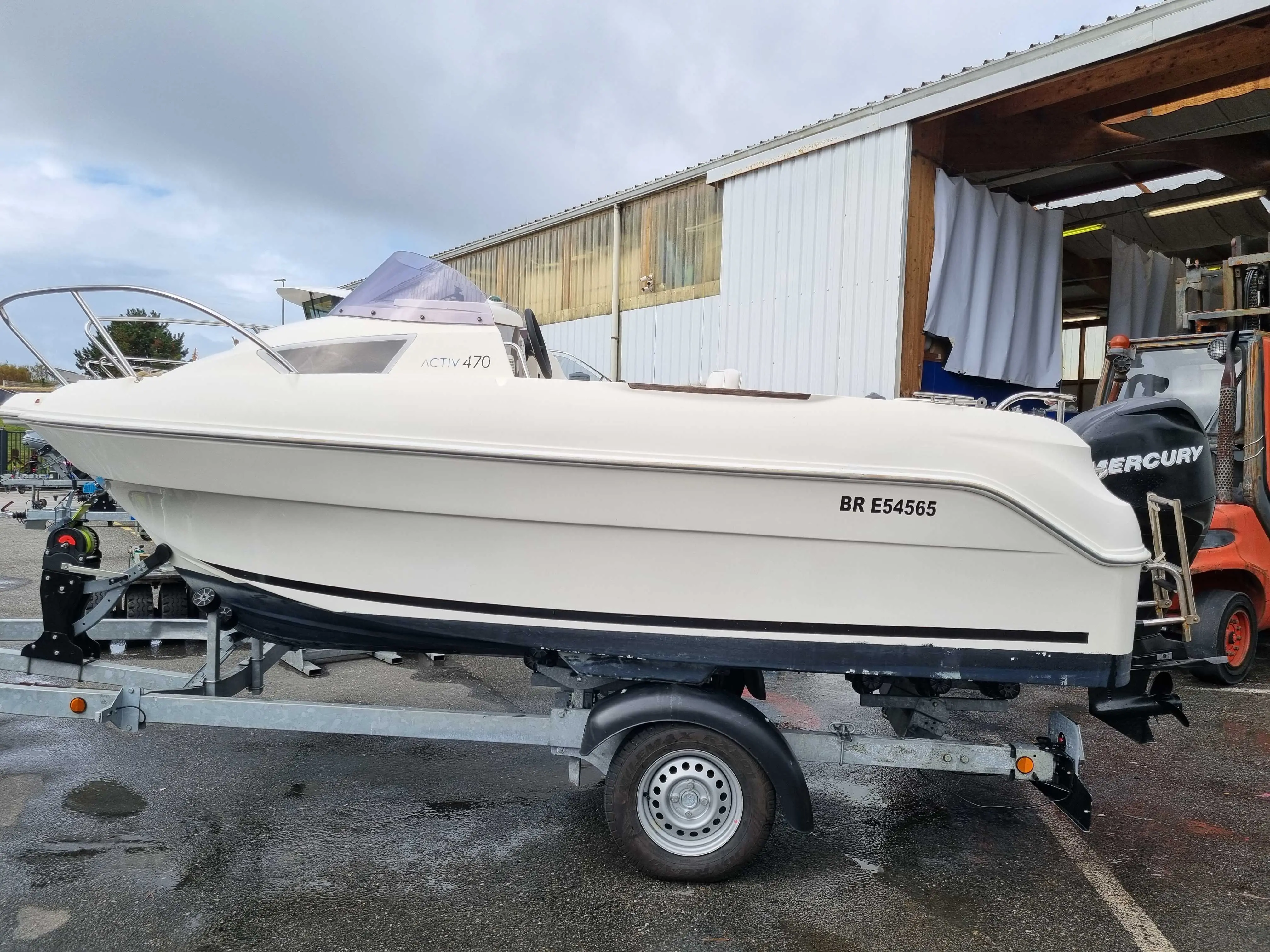 Quicksilver Activ 470 Cabin — Bateau blanc vu de profil sur remorque devant un hangar