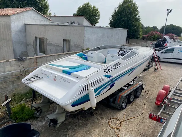 Wellcraft Scarab 29 — Bateau à moteur blanc et bleu présenté sur une remorque dans une cour.
