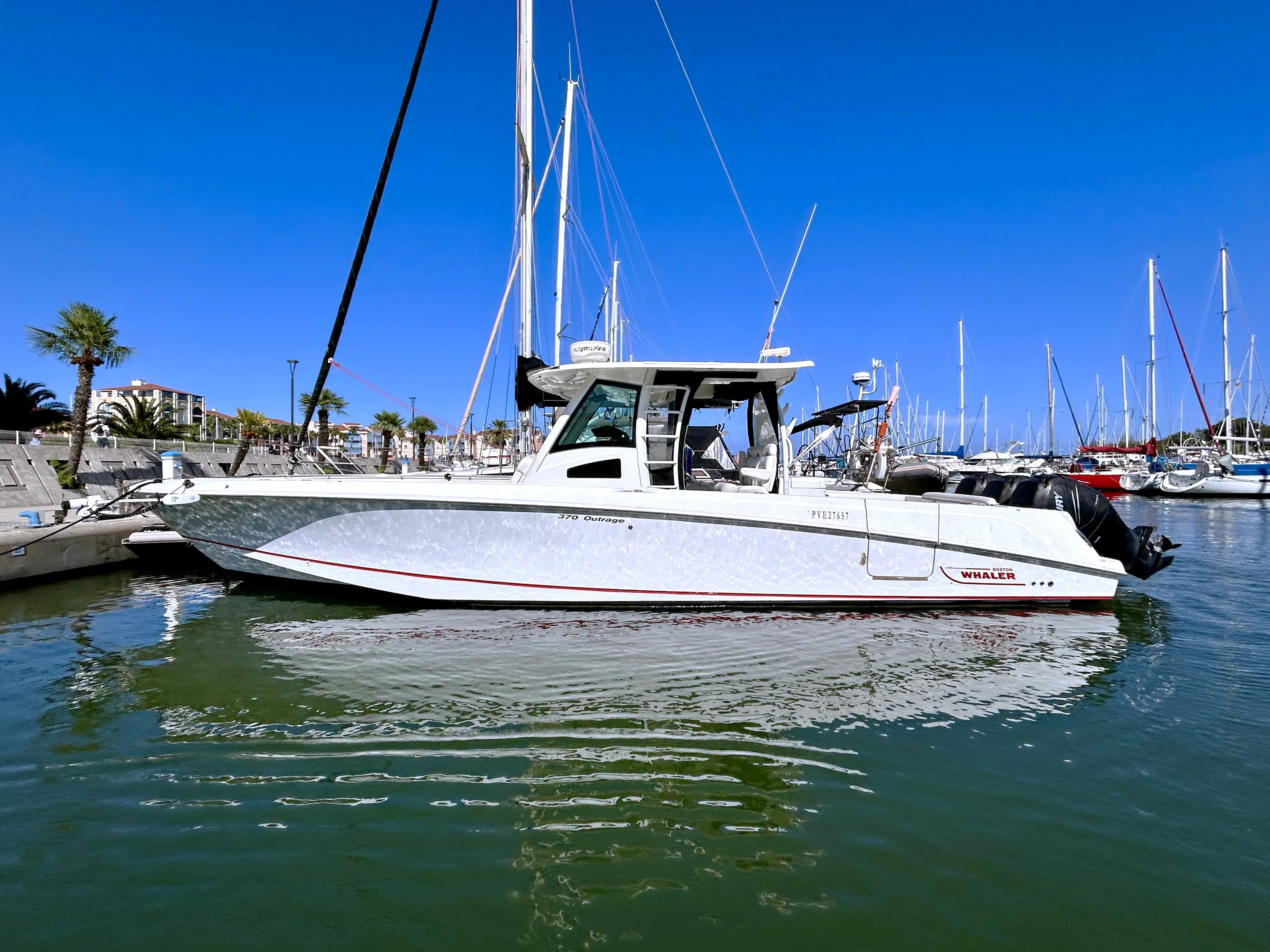 Boston Whaler 370 Outrage — Bateau à moteur blanc vu de profil dans un port, entouré de voiliers.