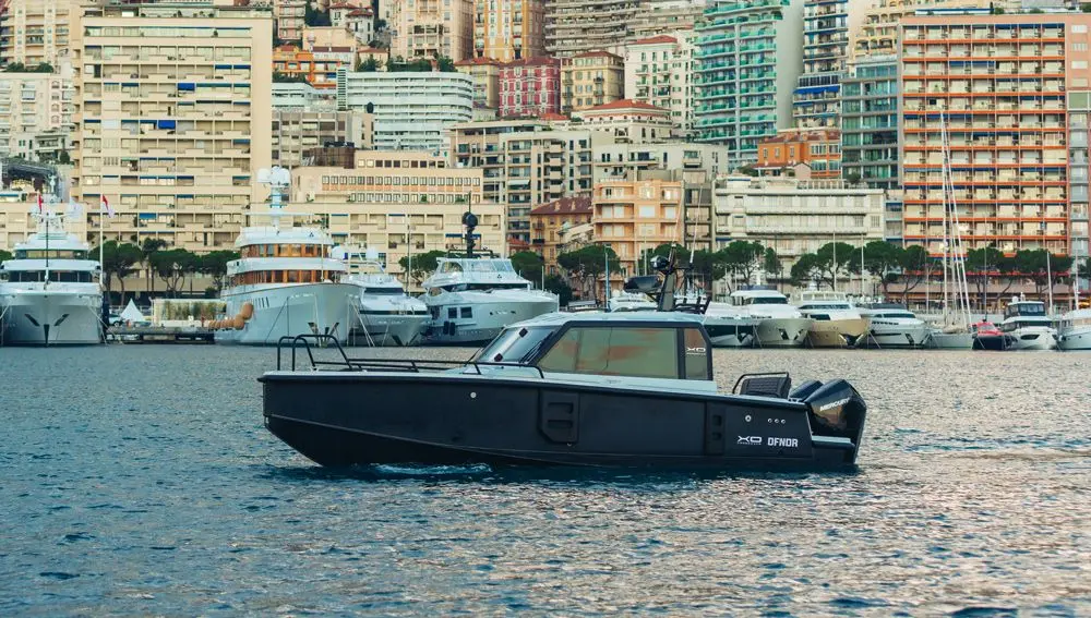 XO Boats DFNDR 8 — Bateau à moteur noir vu de profil dans un port, devant des immeubles côtiers.