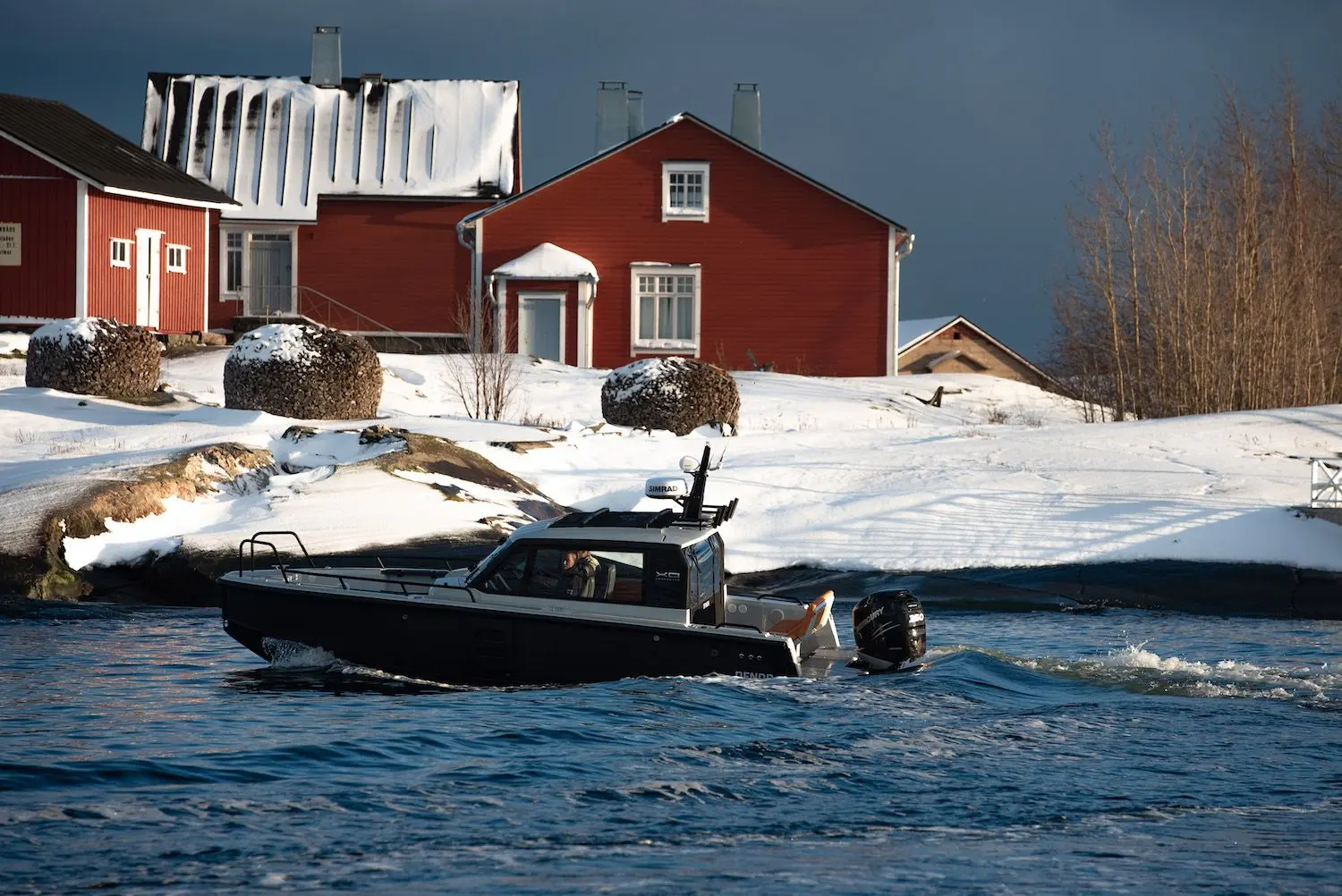 XO Boats DFNDR 8 — Bateau à cabine naviguant devant des maisons enneigées.
