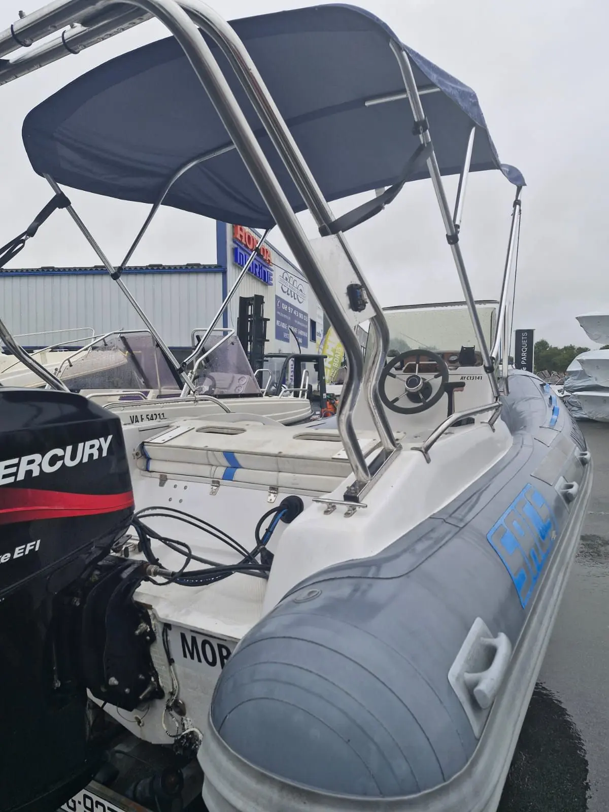 Sacs S 475 — Bateau pneumatique à console avec moteur hors-bord et taud dans un chantier nautique.