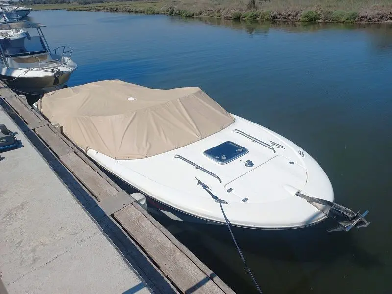 Jeanneau Runabout 755 — Bateau blanc amarré, vu de trois quarts depuis le quai, avec taud beige.