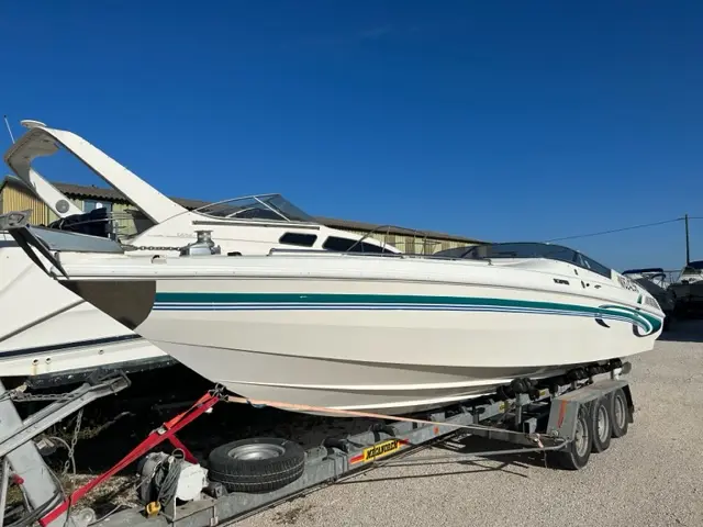 Wellcraft Scarab 29 — Bateau à moteur blanc à bandes turquoise présenté sur une remorque dans un parc nautique.