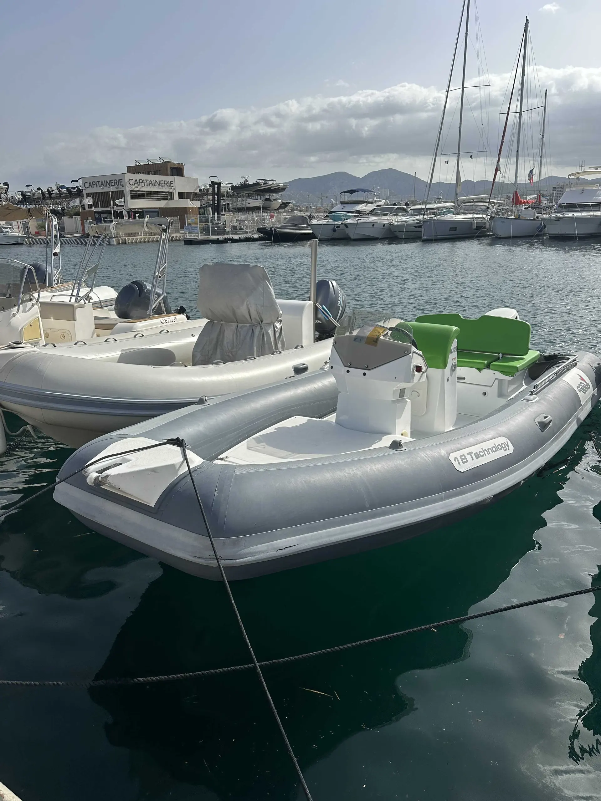 MV Marine 18 — Semi-rigide gris amarré dans un port, avec d'autres bateaux en arrière-plan.