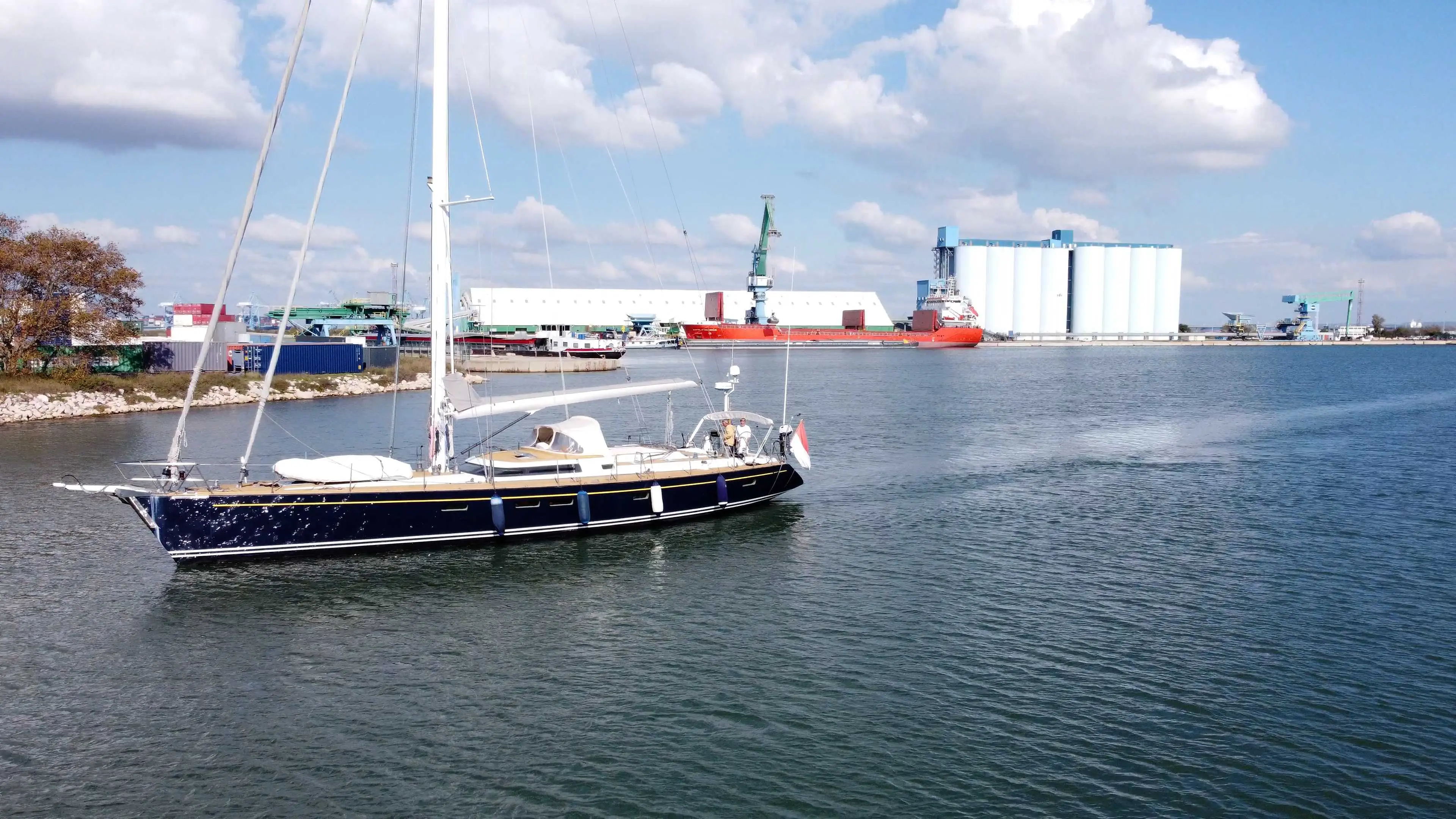 Cnb 70 — Voilier bleu et blanc naviguant devant des installations portuaires.