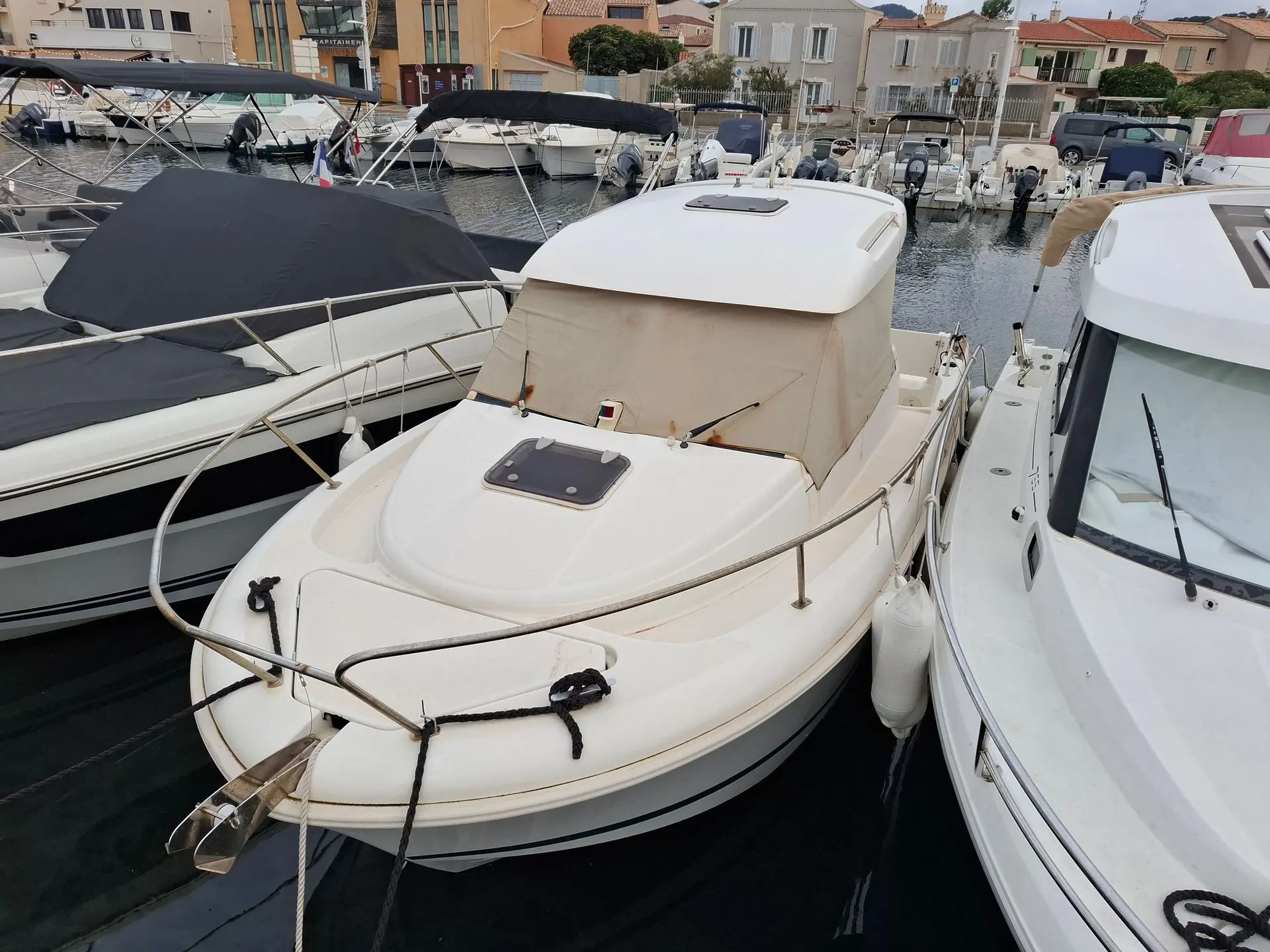 Jeanneau Merry Fisher 655 — Bateau à moteur amarré, vu de l’avant entre deux embarcations au port.