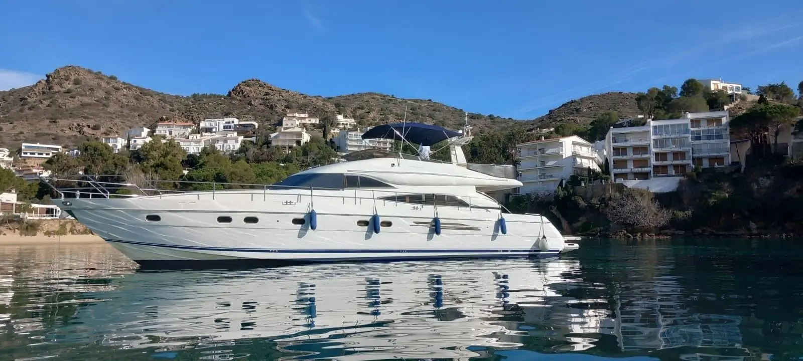 Princess 65 Fly — Vedette blanche amarrée dans une baie, avec des habitations sur les collines.