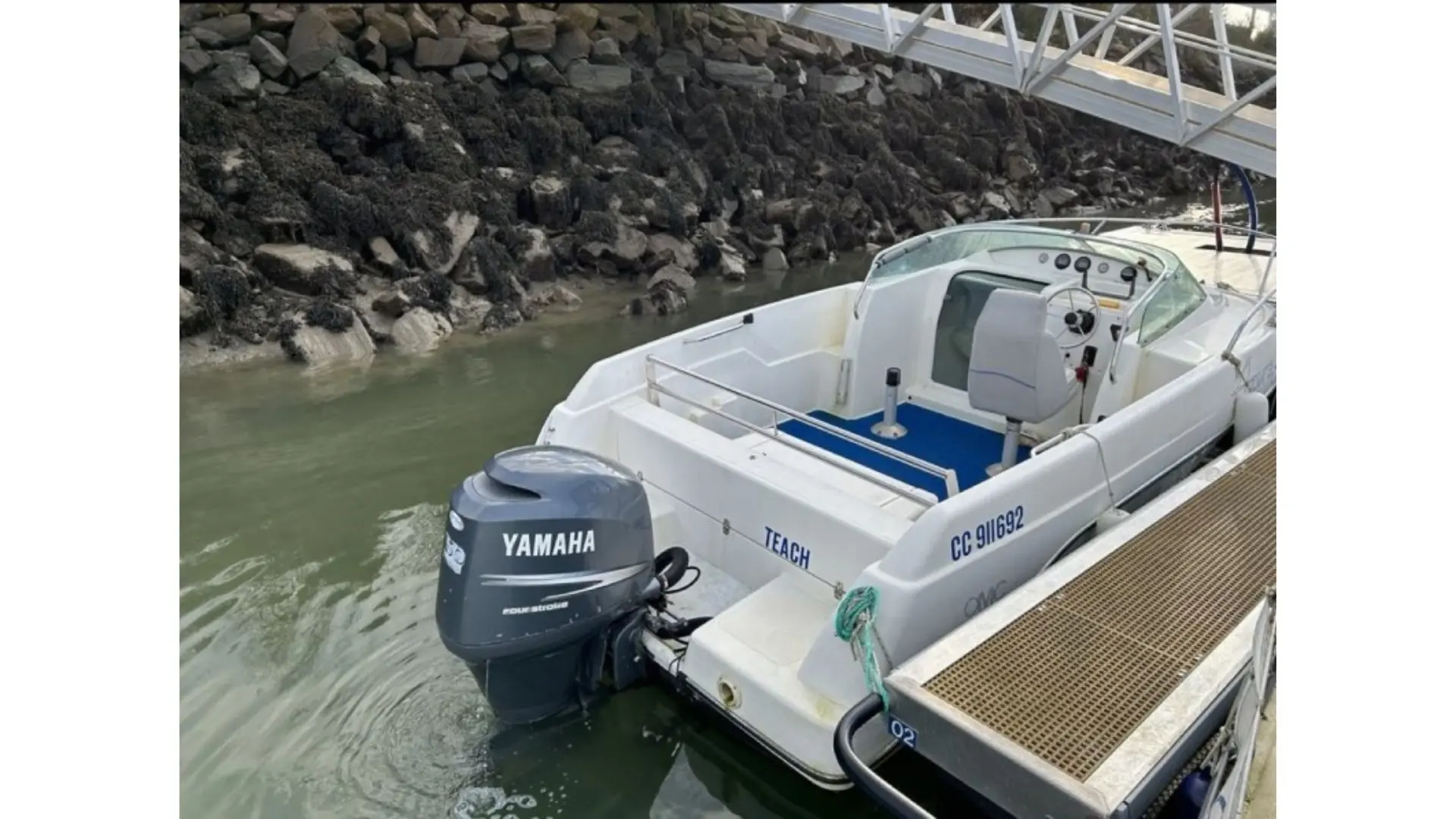 Kelt Azura 600 — Bateau à moteur blanc amarré à un ponton, vu de trois quarts arrière.