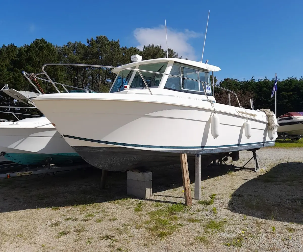 Jeanneau Merry Fisher 655 — Vedette blanche à cabine photographiée à terre, entourée d’autres embarcations.