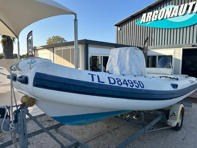 Lomac Beluga 18 — Bateau pneumatique blanc et bleu présenté sur sa remorque devant un bâtiment.