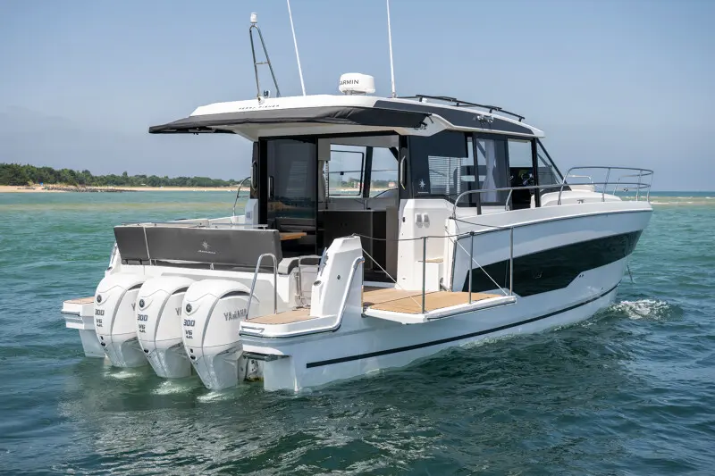 Jeanneau Merry Fisher — Bateau à moteur blanc à trois hors-bord naviguant près du littoral.