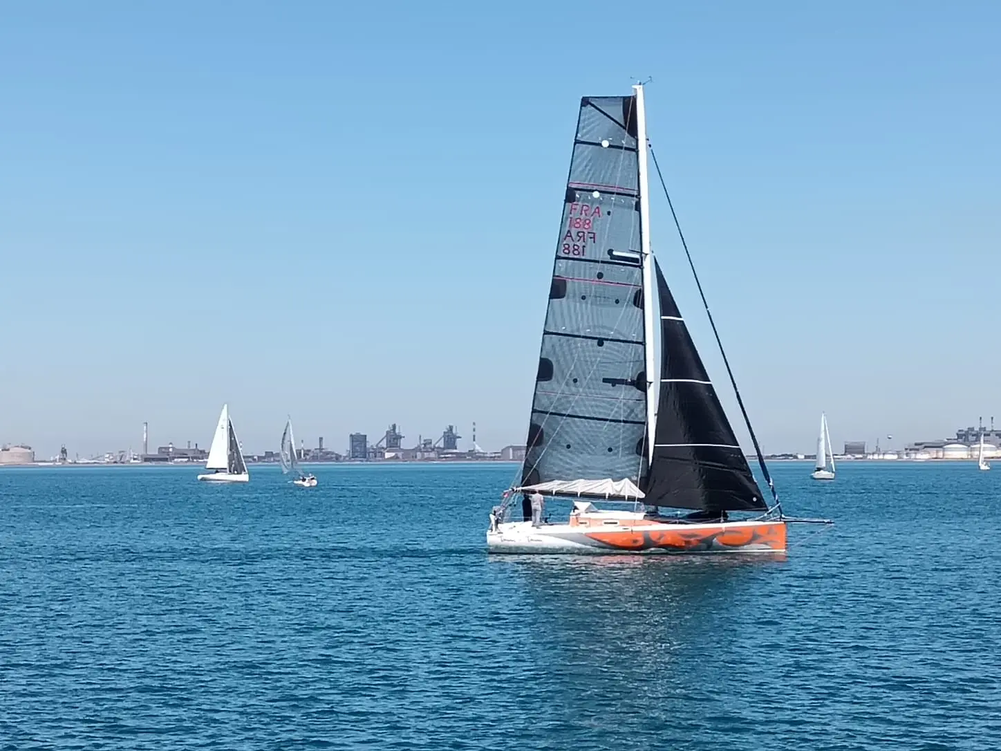 Pogo Structures Pogo 40 — Voilier orange et blanc naviguant sous voiles, avec plusieurs bateaux en arrière-plan.