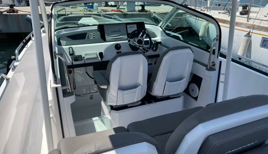 Axopar 28 T Top — Vue du poste de pilotage avec deux sièges, volant et écran de navigation.