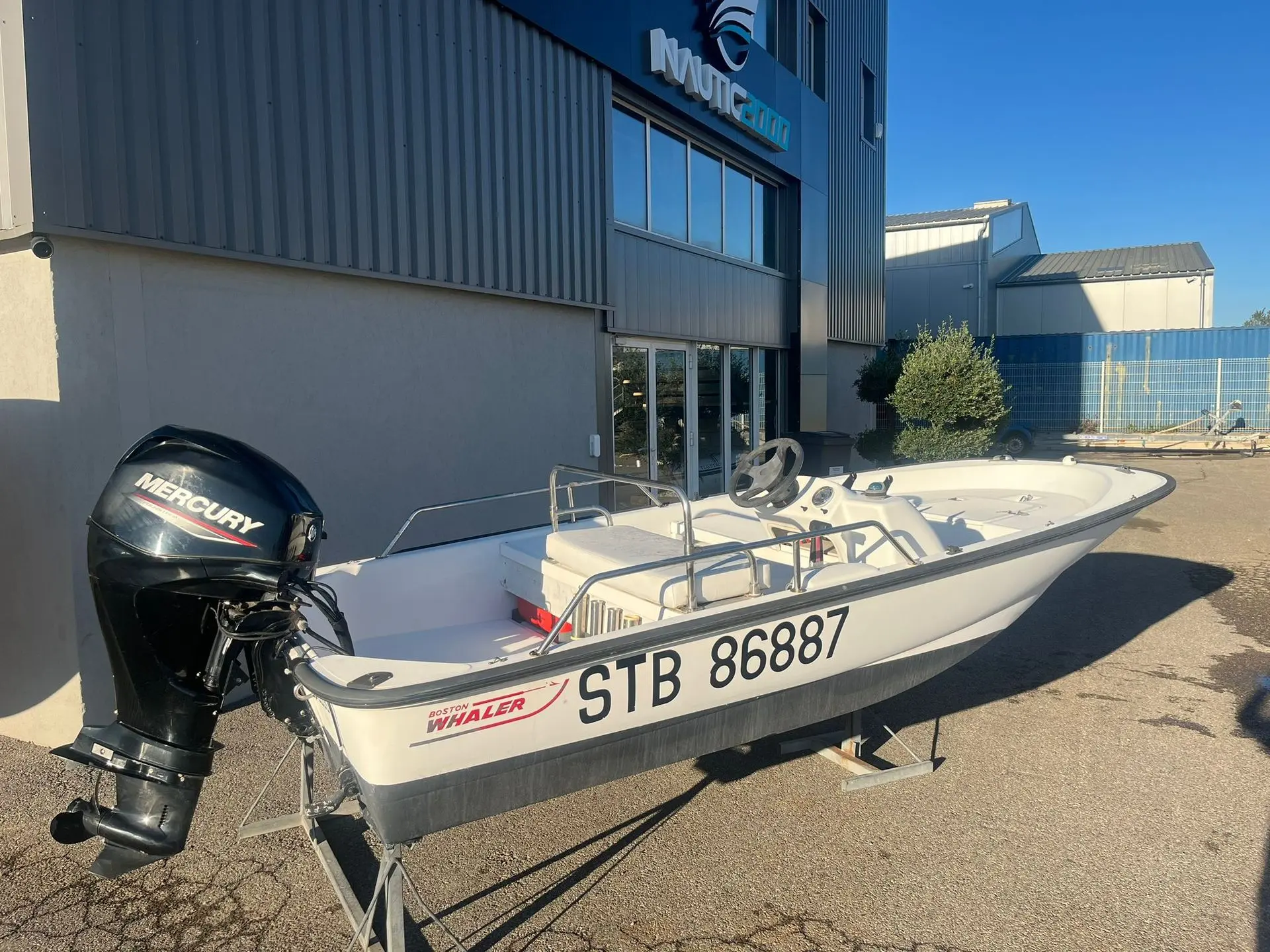 Boston Whaler 13 — Bateau à moteur blanc photographié sur sa remorque devant un bâtiment.
