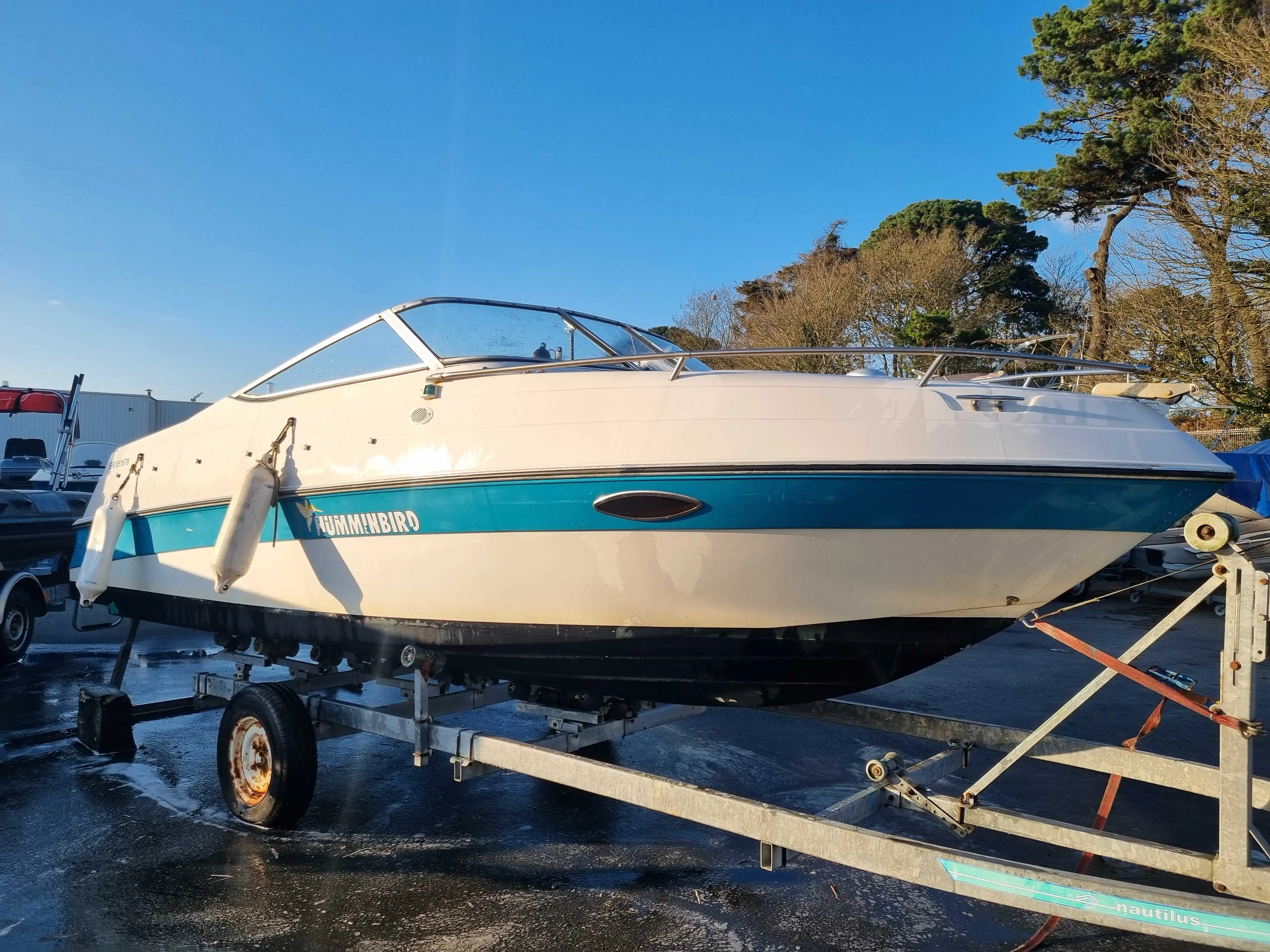 Four Winns Sundowner 195 — Bateau à moteur bleu et blanc posé sur une remorque, vu de profil latéral.