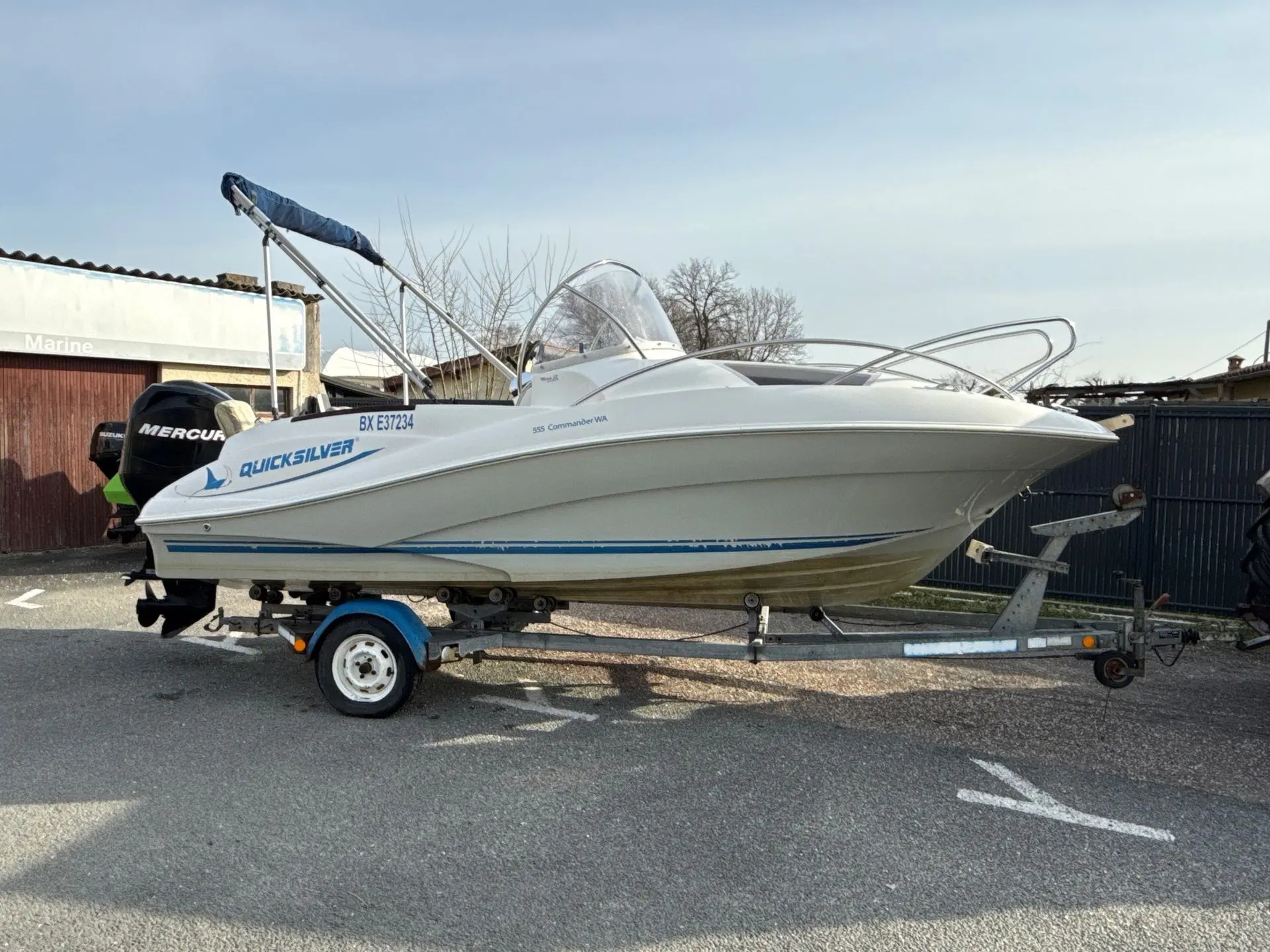 Quicksilver 555 Commander — Bateau à moteur blanc photographié de profil sur sa remorque, à l'extérieur.