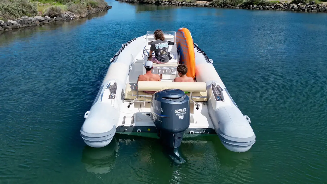 Zodiac Sea Hawk 700 — Vue arrière d’un bateau semi-rigide avec trois personnes à bord sur une eau calme.