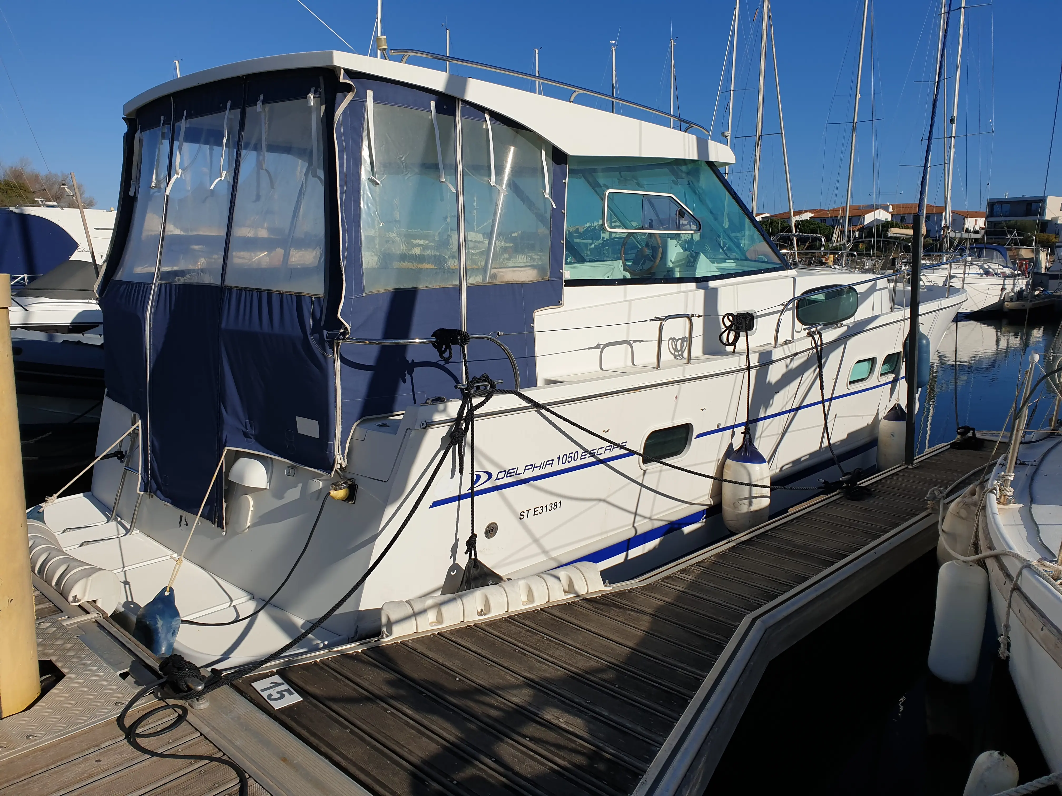 Delphia 1050 Escape — Bateau à moteur blanc amarré dans une marina, vu de trois quarts arrière.