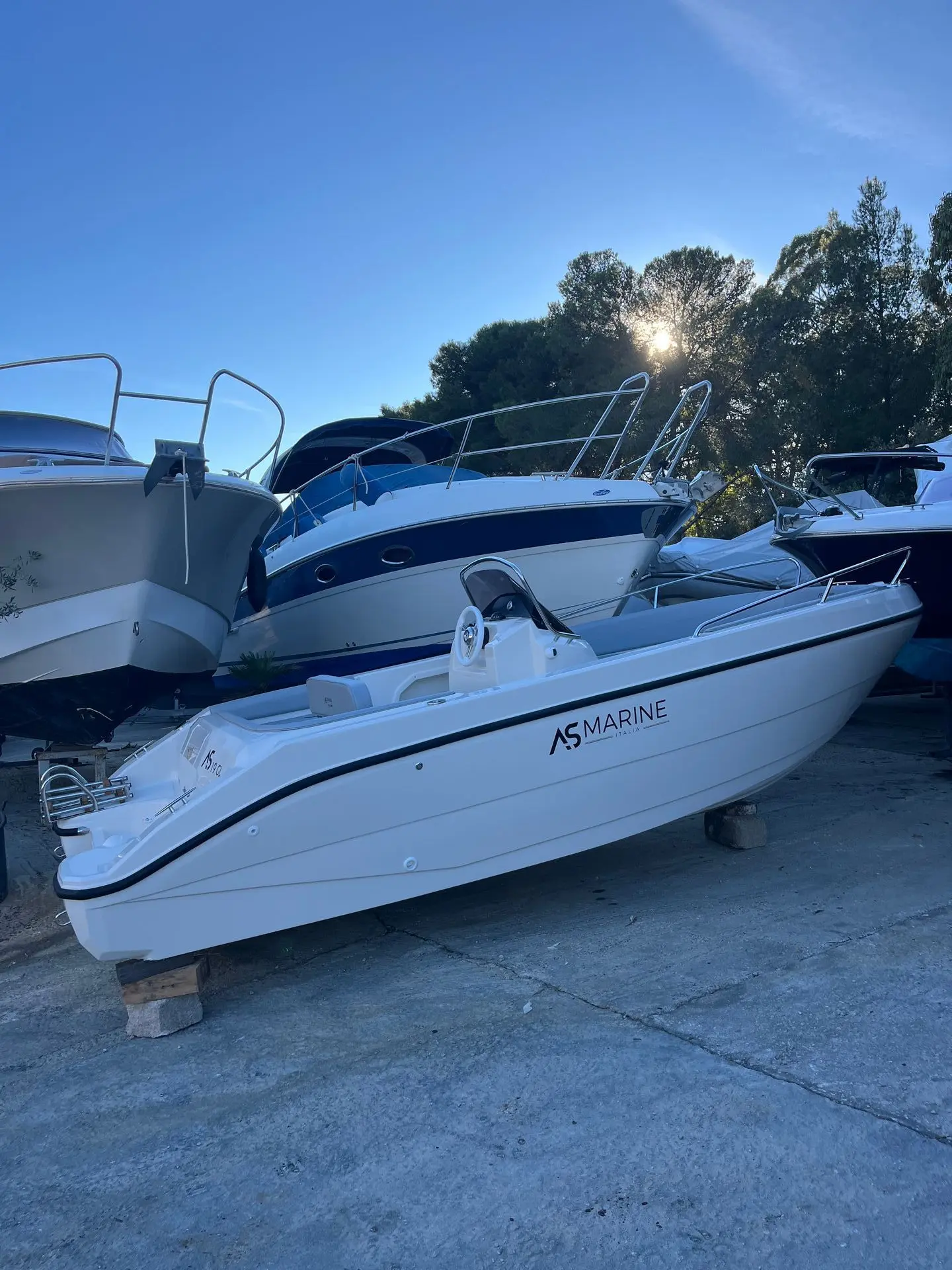 Eolo AS 19GL OPEN — Bateau à moteur blanc et bleu photographié à terre parmi d'autres embarcations.