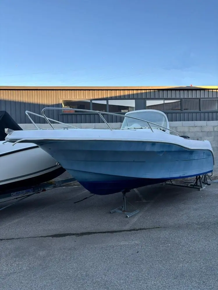 Quicksilver 630 Open Commander — Bateau à moteur bleu et blanc présenté à terre devant un hangar.